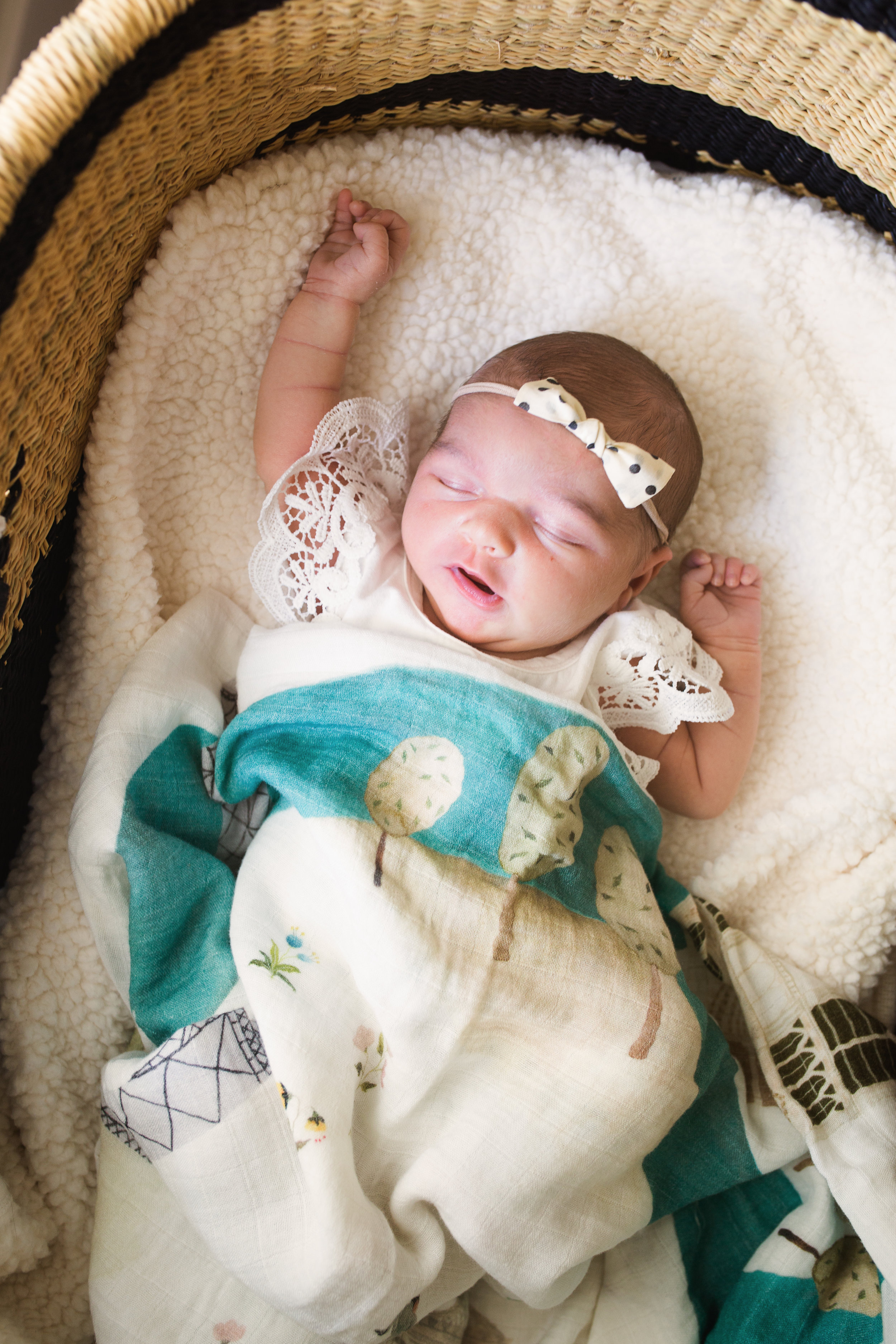 newborn baby girl in bassinet sleeps with one arm above her head