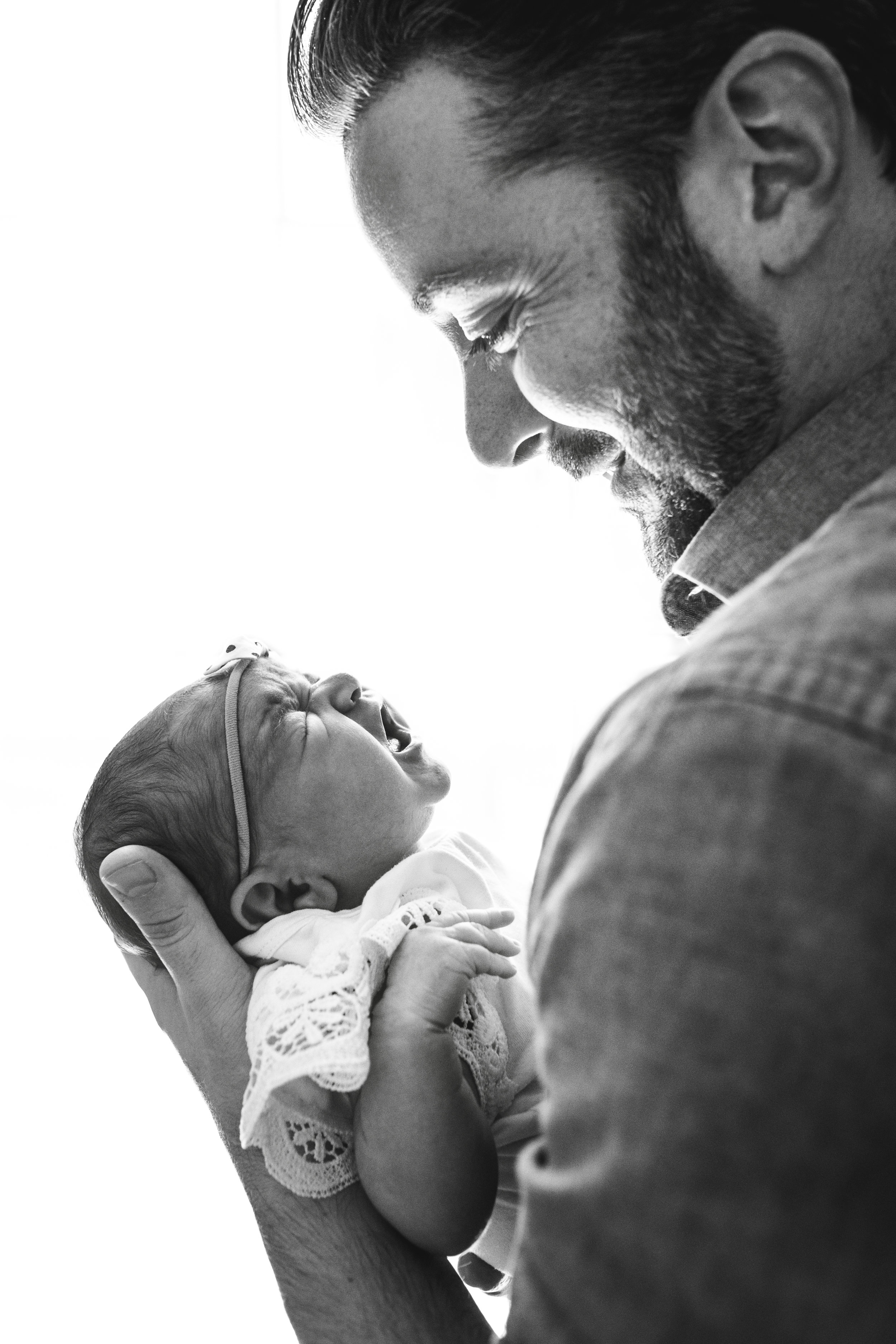 black and white photograph of father smiling at crying baby girl