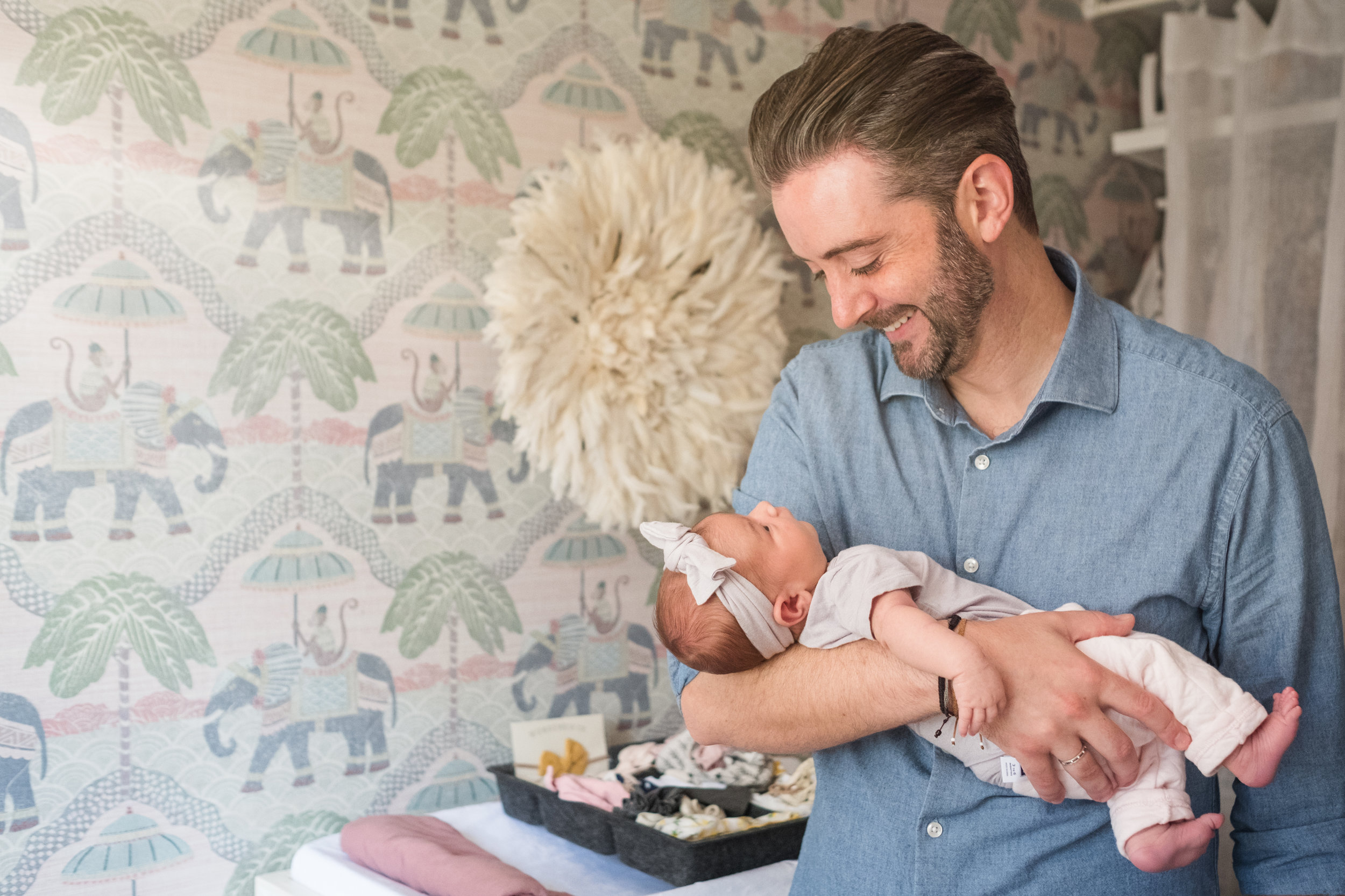 happy, joyful new father smiles while holding infant daughter in her nursery