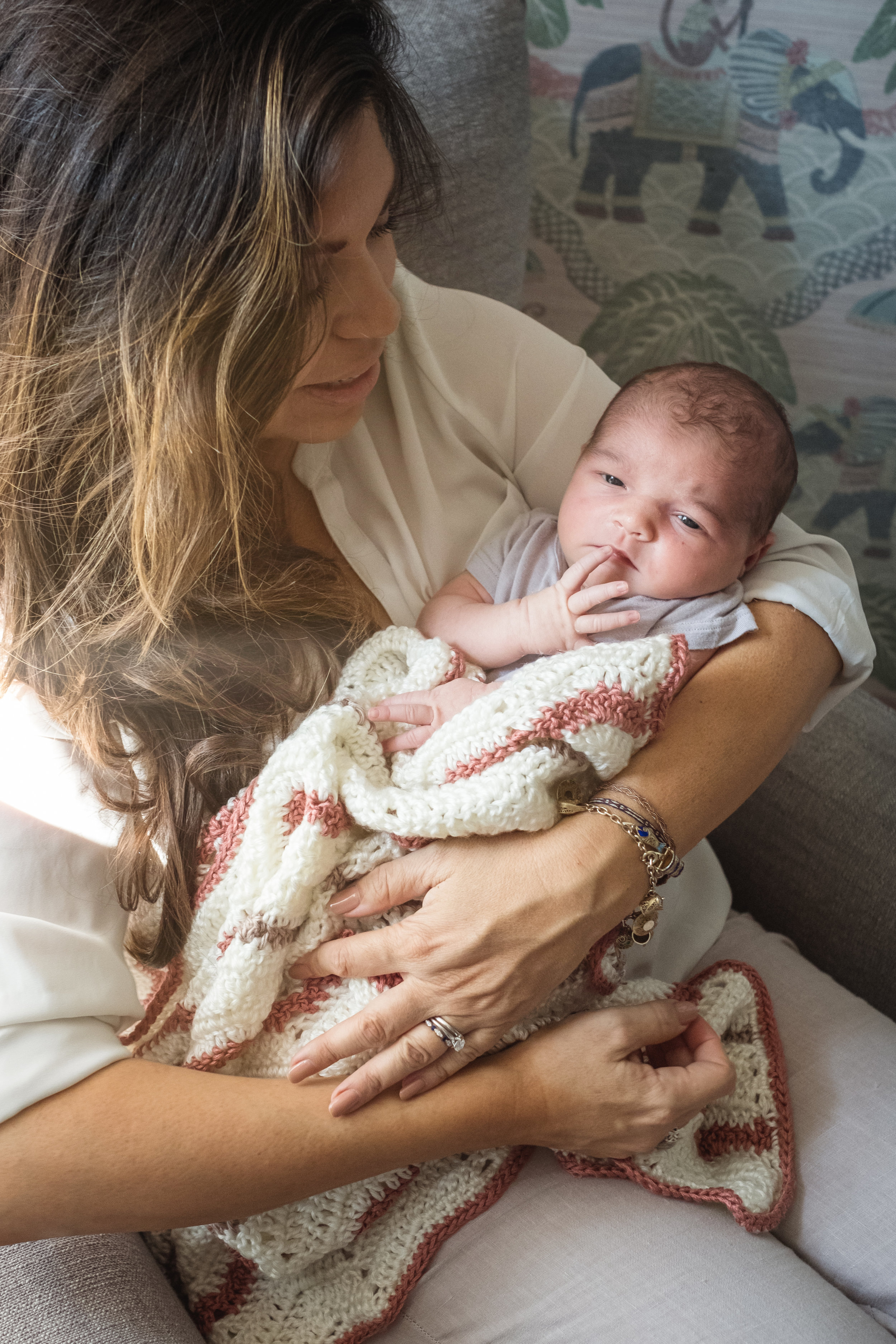 seated mother cuddles newborn daughter who looks at camera in photograph