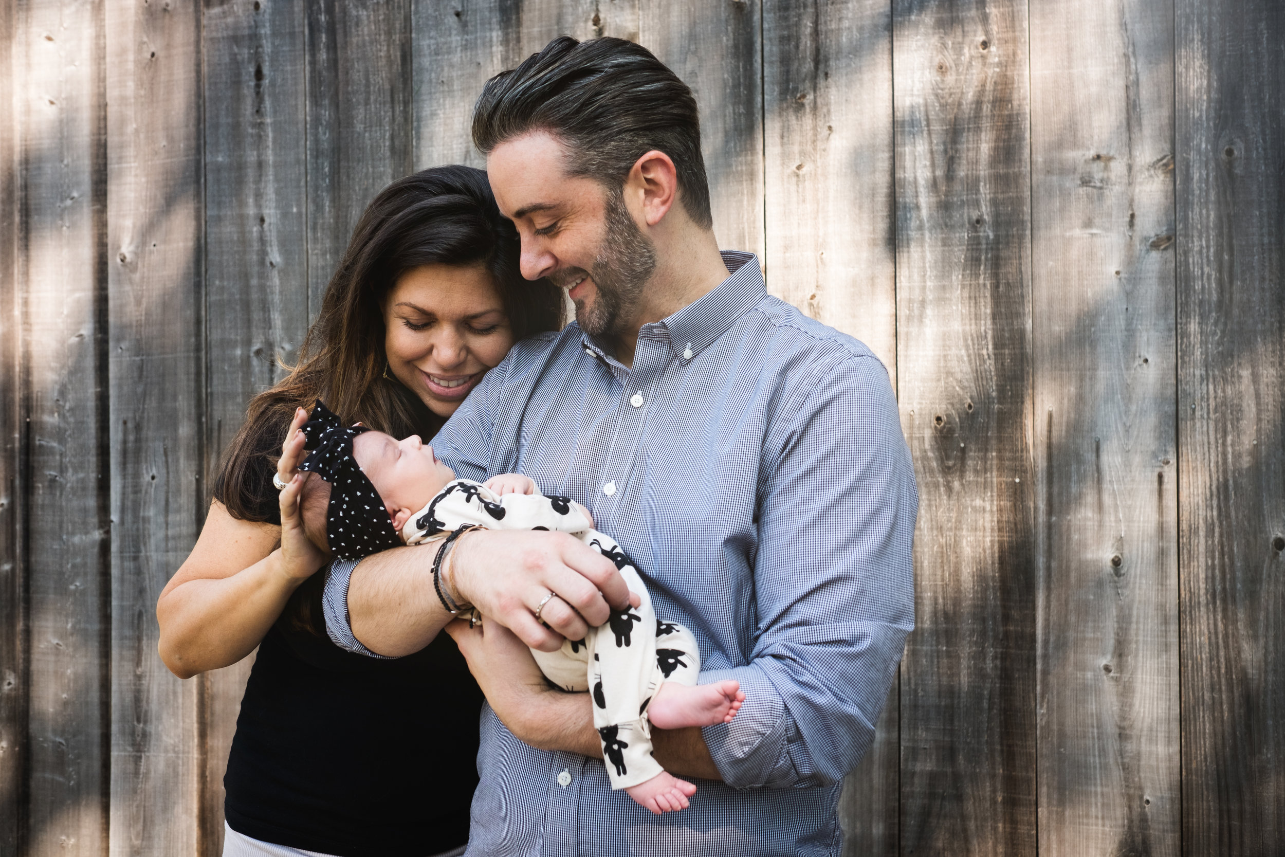 outside portrait of parents holding newborn baby daughter by wood doors of garage