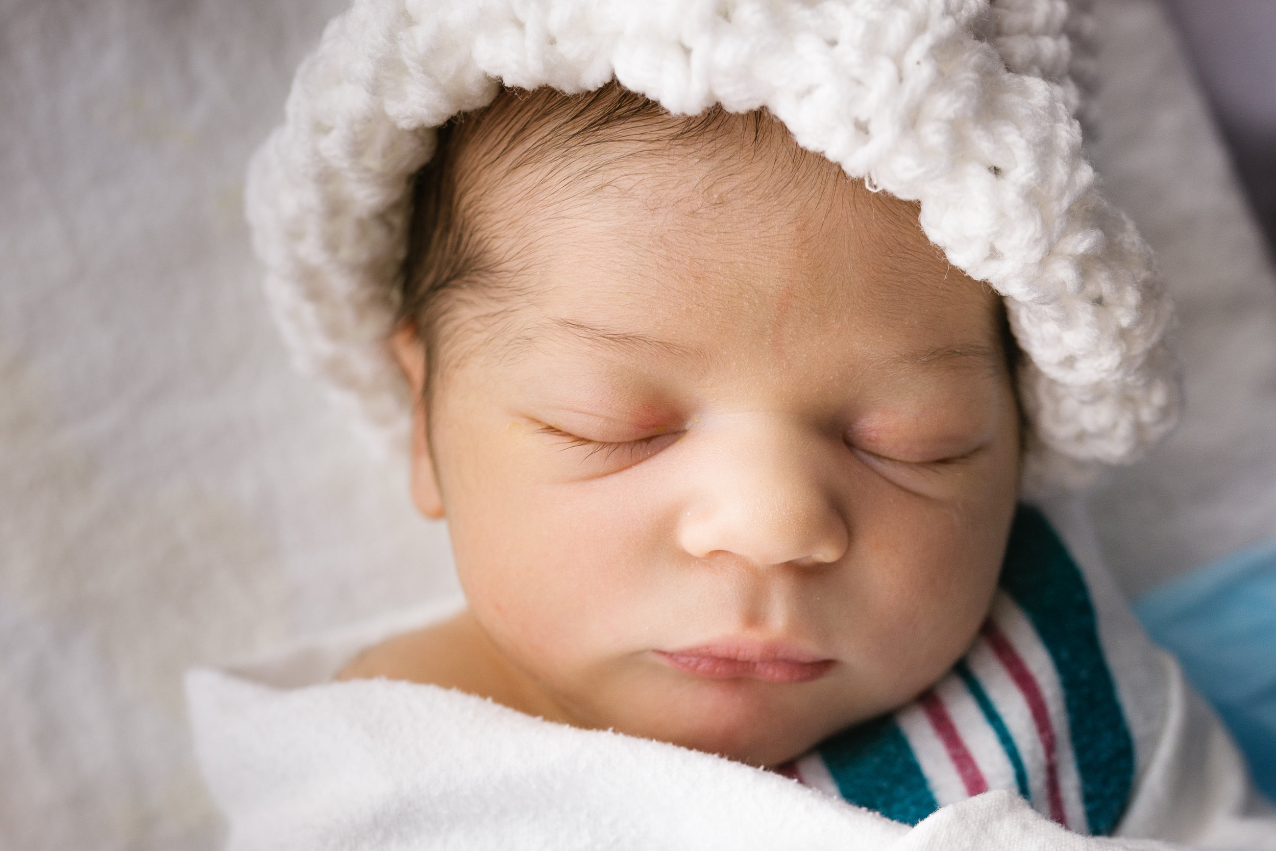 close up photograph of newborn baby boy's face wearing white hat