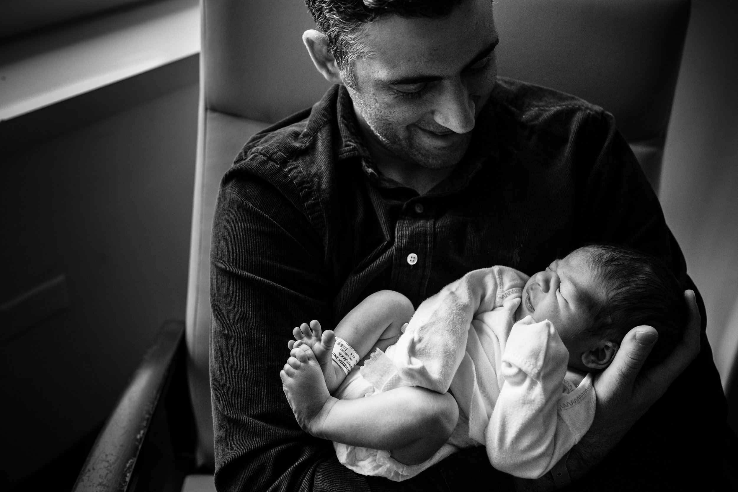 black and white photograph of father smiling at his infant son in Baltimore hospital room