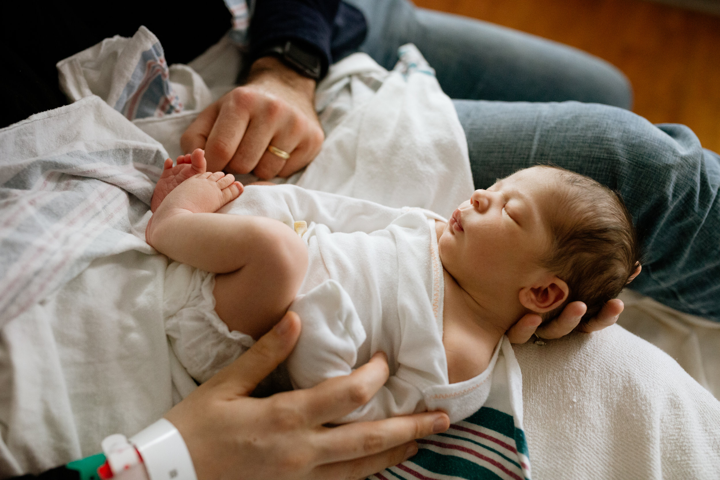 beautiful backlit portrait of newborn baby in parents lap wearing white onesie