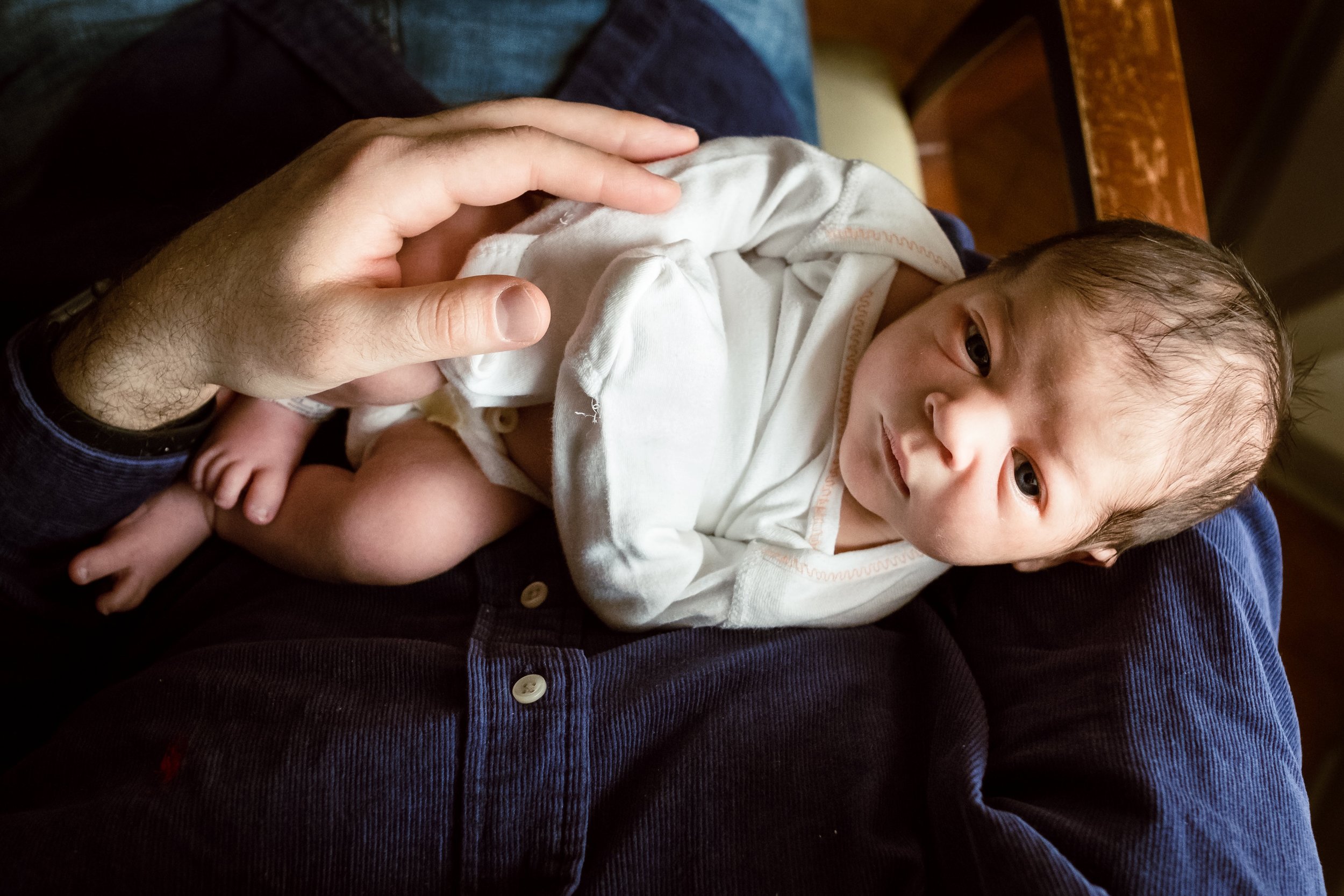 infant baby boy in father's arms looking at camera