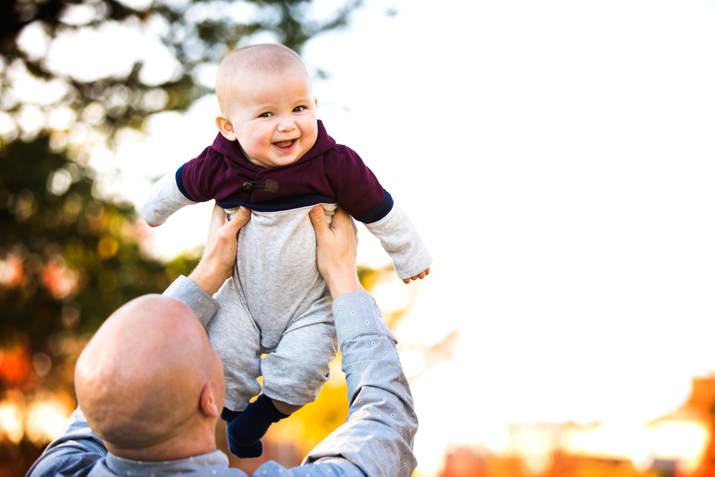 photograph taken while dad holds grinning baby son up in the air 