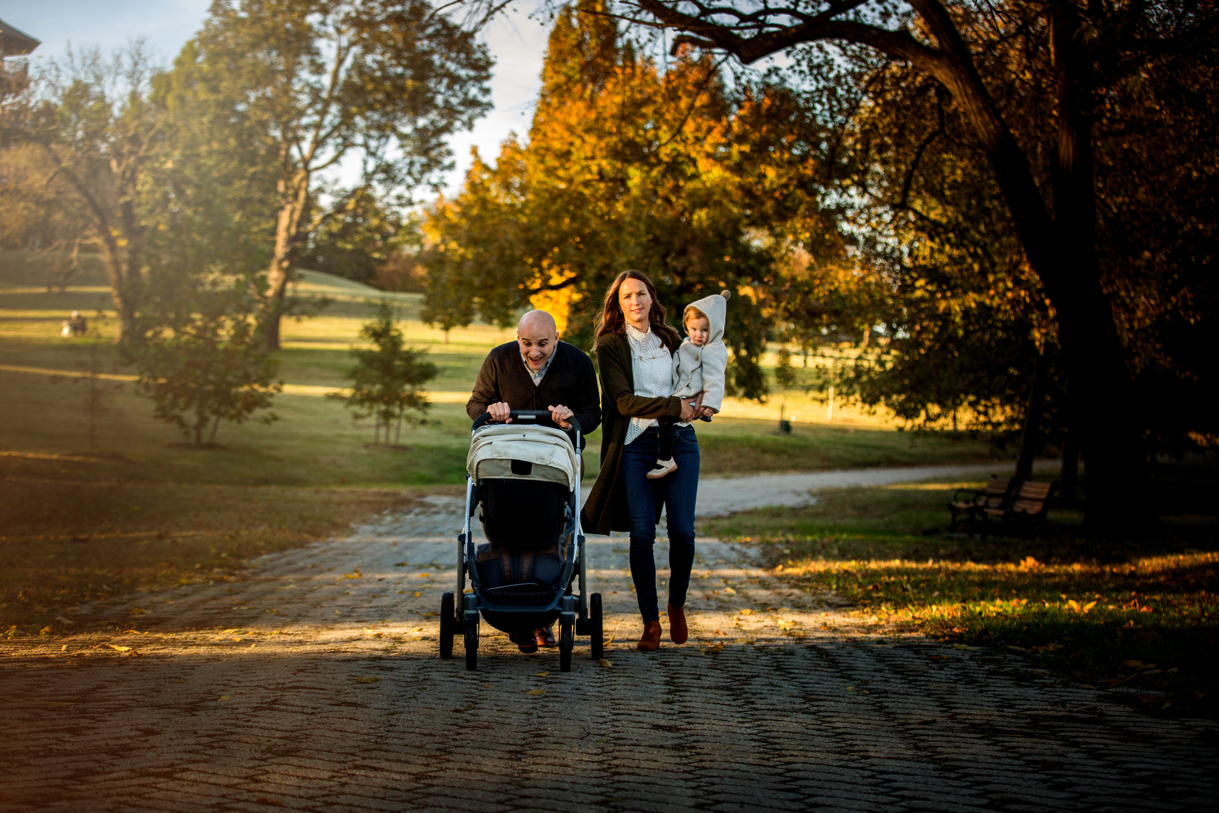 family of four with stroller walking through Baltimore park path in fall