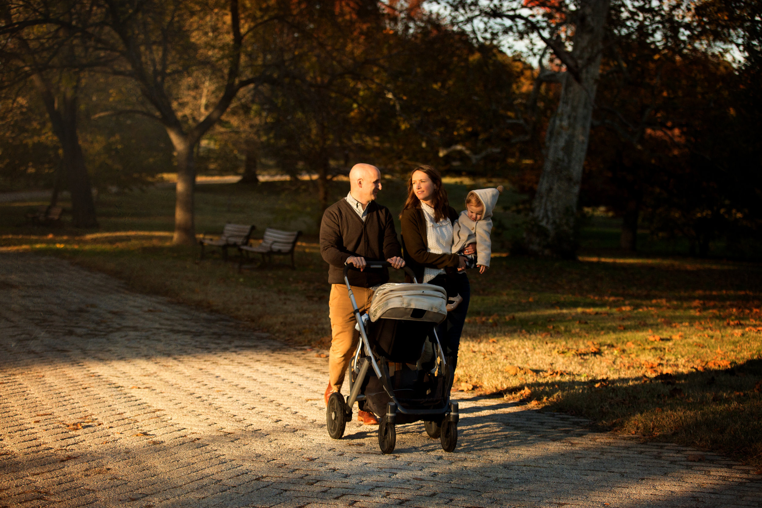 parents and children walking with stroller in evening with sunlight on sidewalk