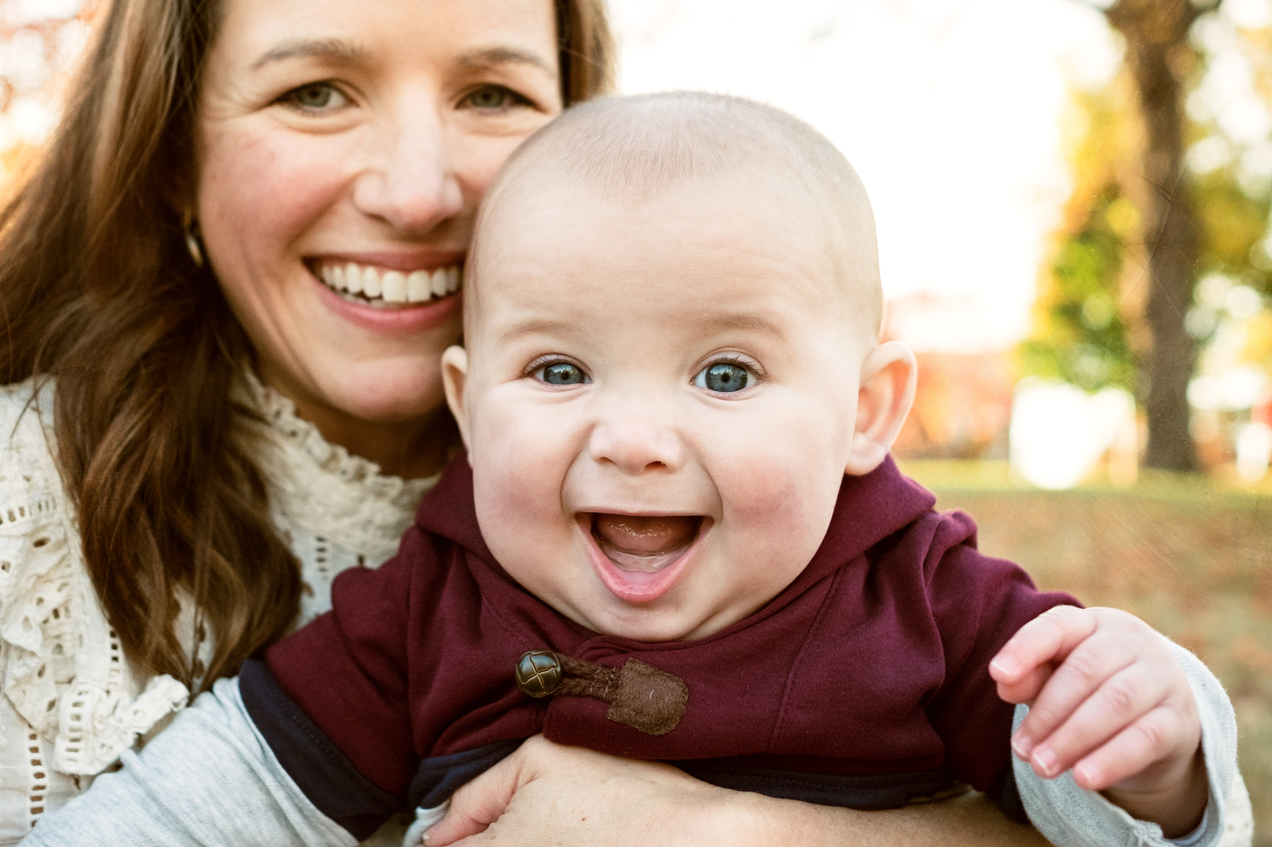 young beautiful mother holds grinning son towards camera for photograph in fall