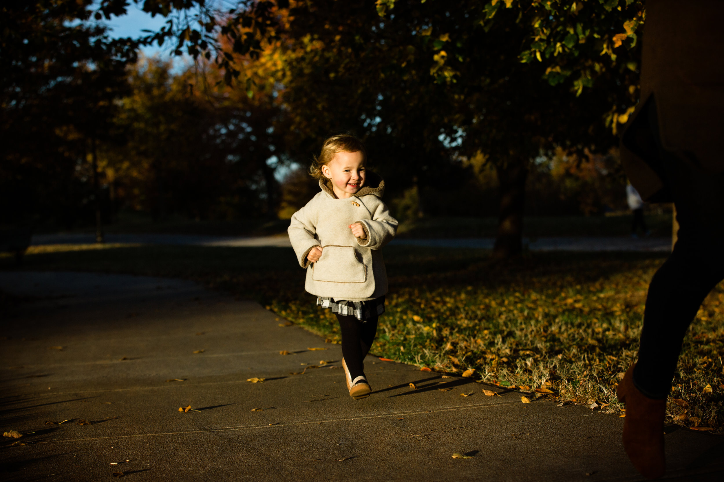 little girl runs along park path with big smile
