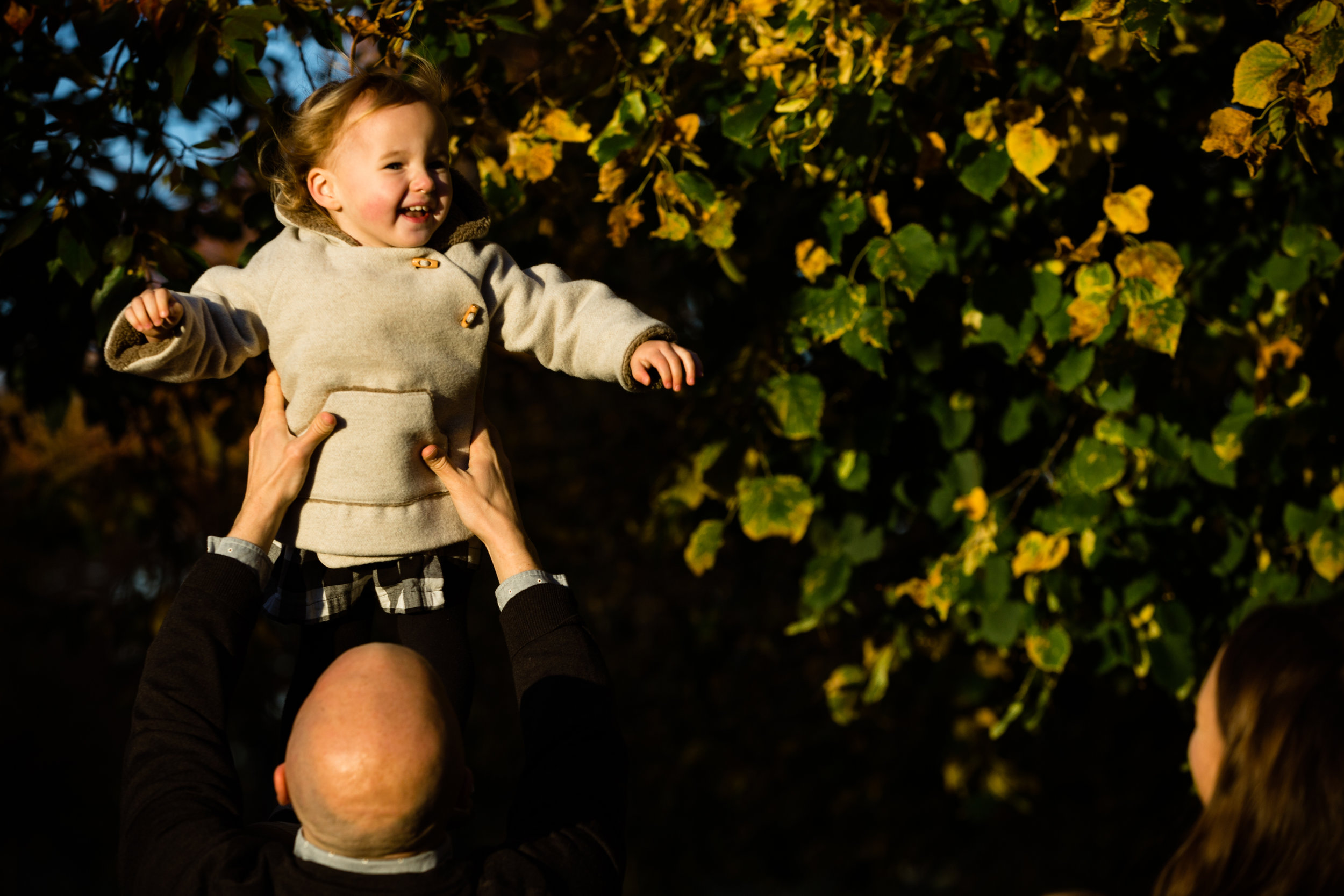 father holds sun lit daughter up in the air in photograph
