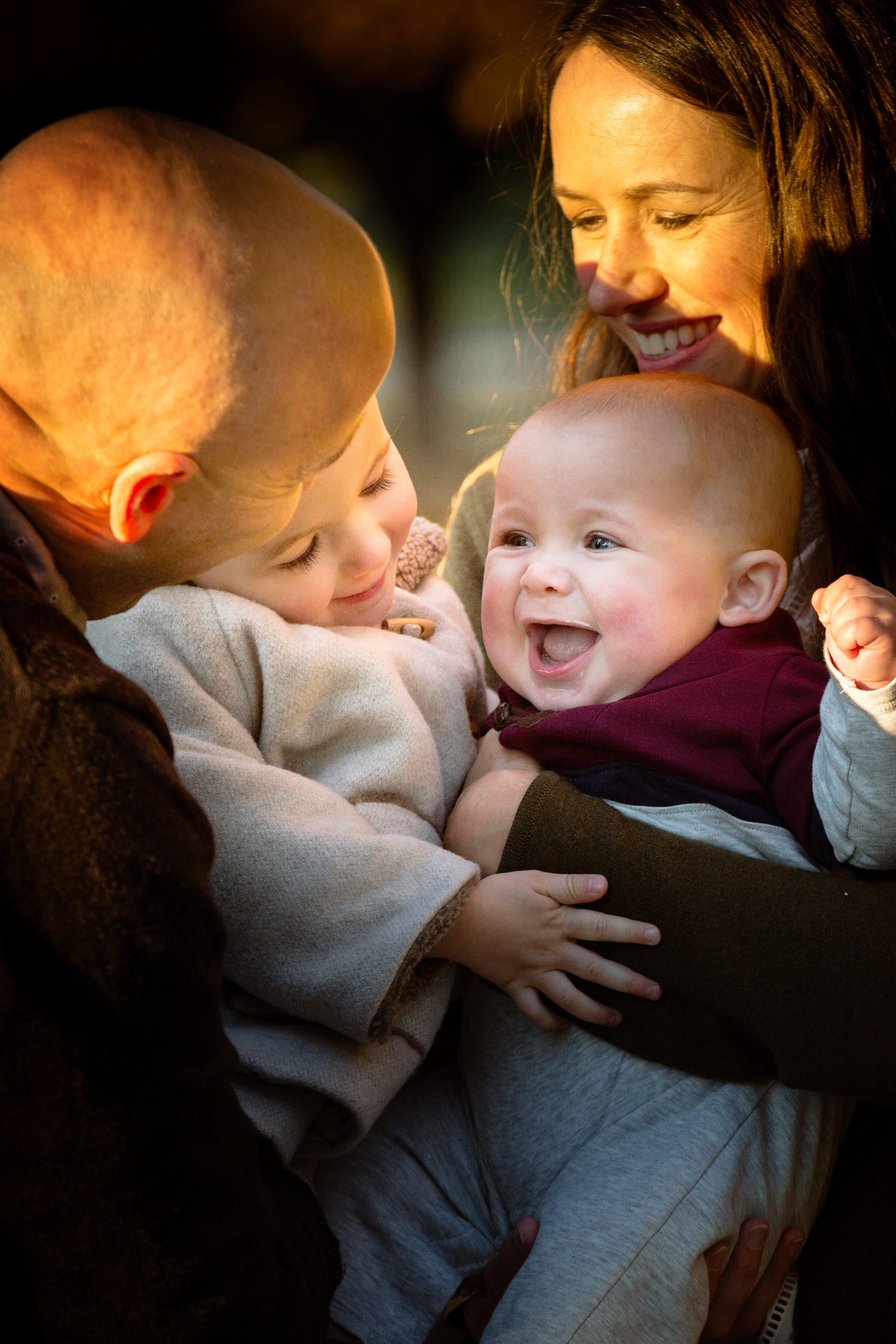 family of four snuggles together and baby son grins