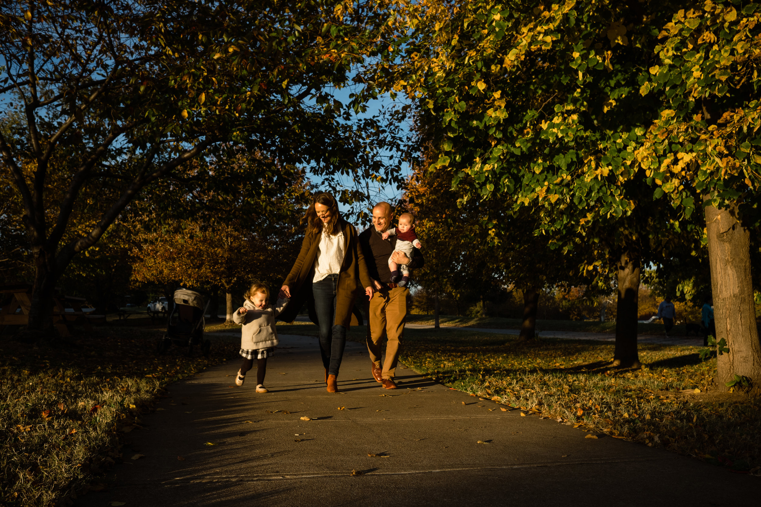 sweet young family with two children walks along golden lit park path