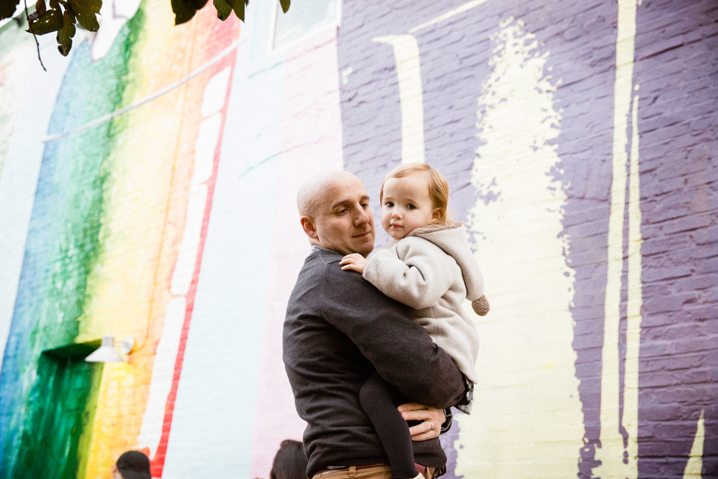 dad holds daughter in front of ice cream shop mural on the streets in the city