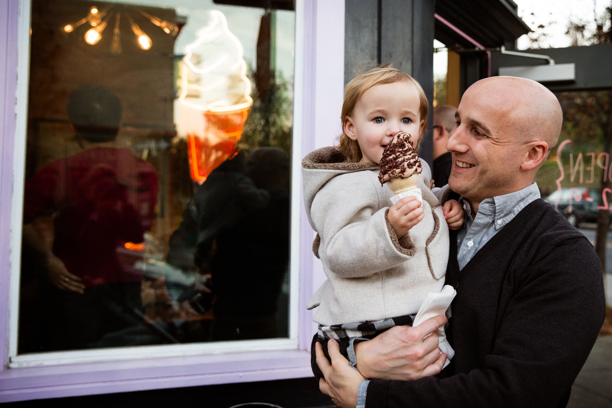 little girl in her father's arms proudly holds up ice cream cone she is eating