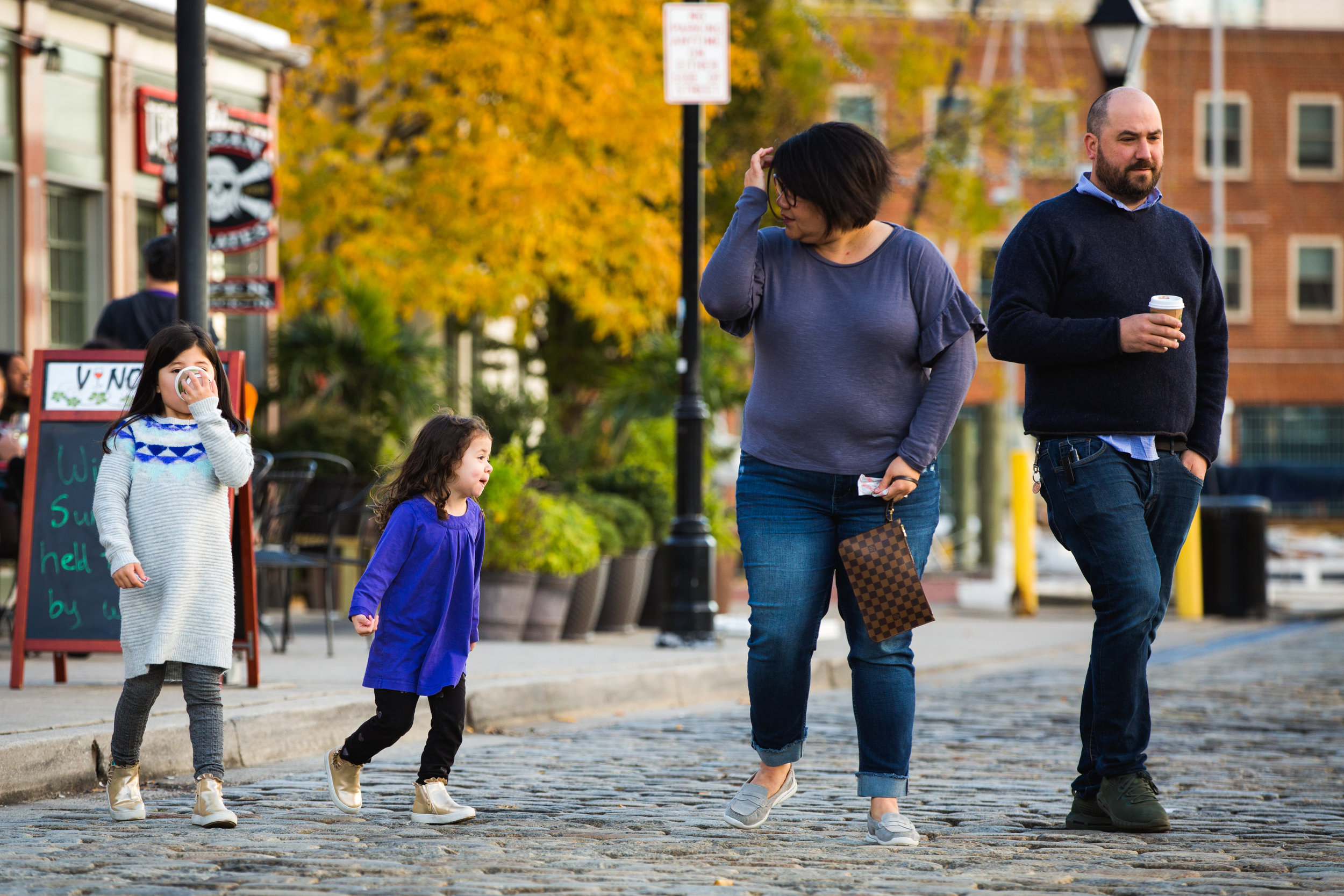 family crosses cobblestone streets in Fells Point neighborhood of baltimore city enjoying a fall evening together