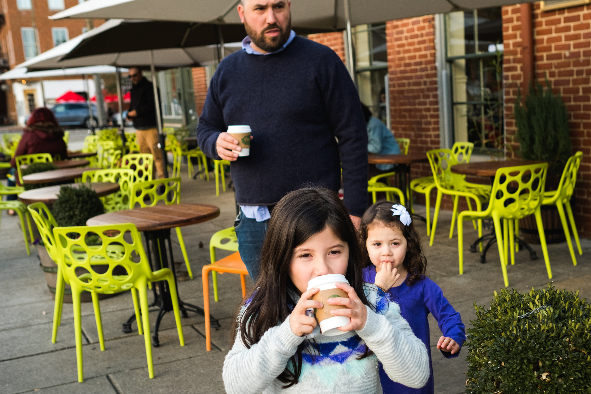 Father and two daughters drinking warm drinks outside cafe in Fells Point