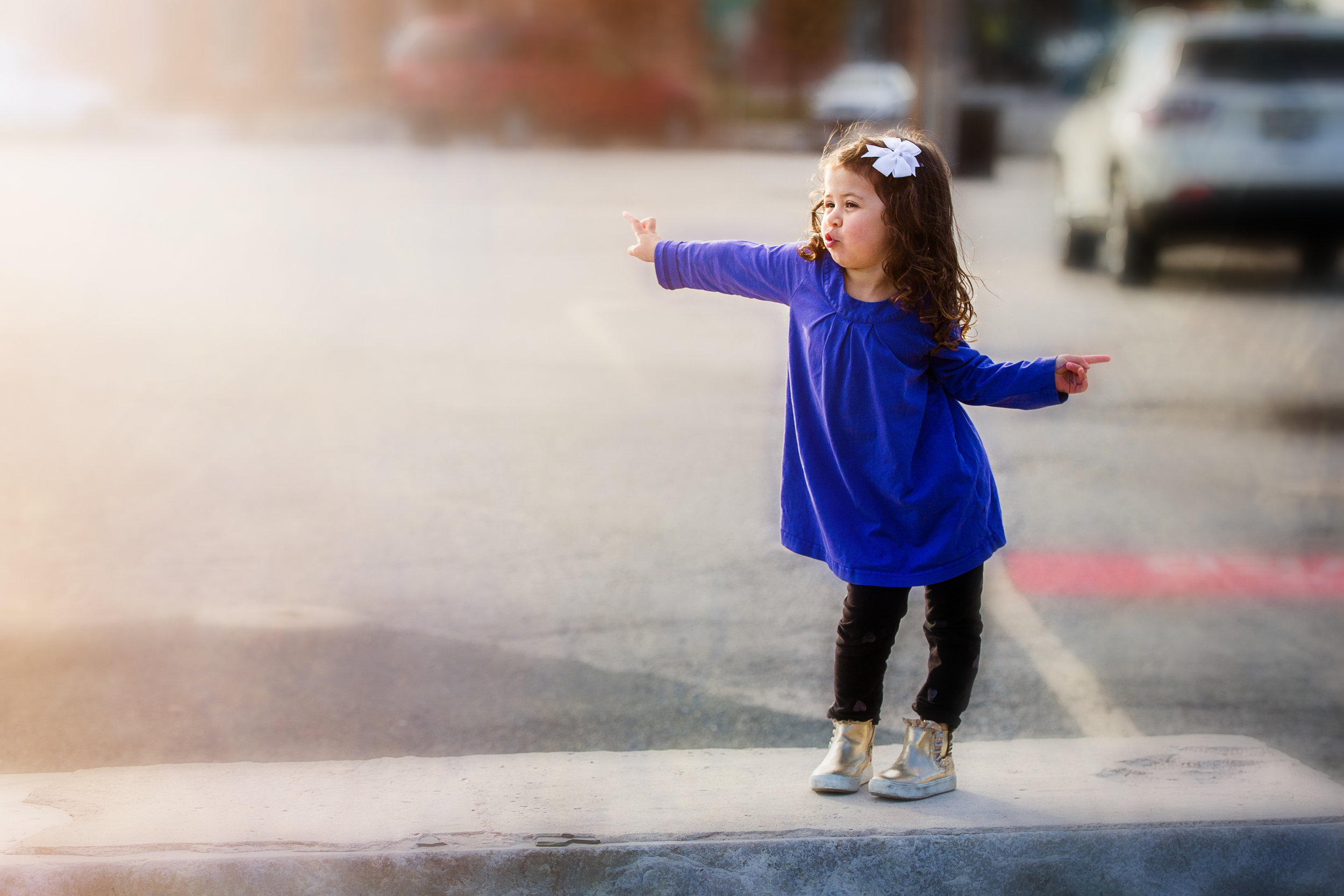 little girl with dark curls dancing in purple dress on city street