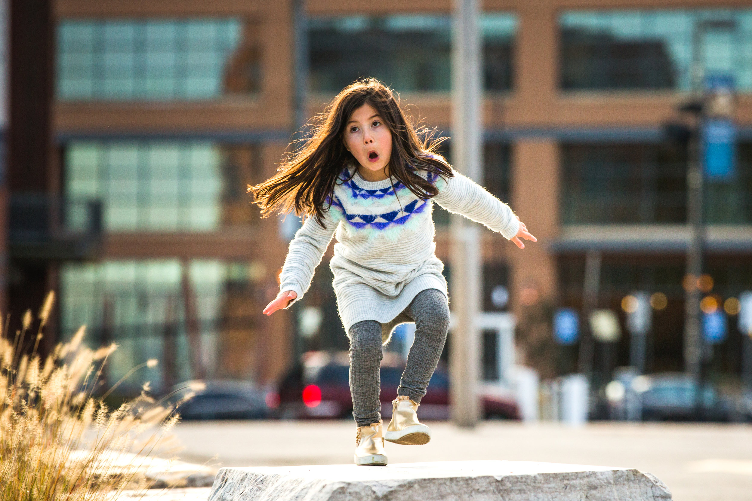 girl with long hair in pretty dress plays by hopping on concrete barrier in the city