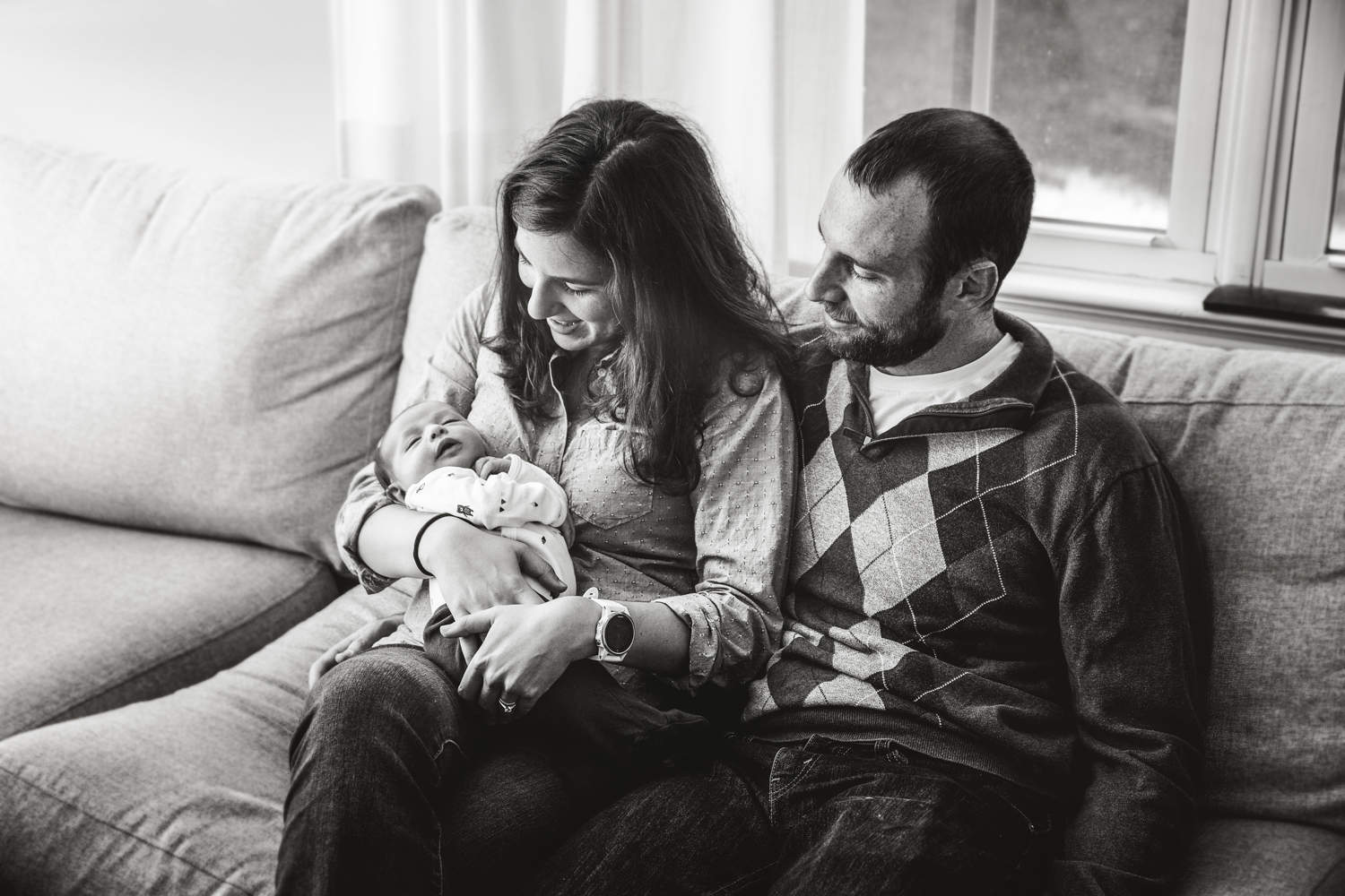parents hold their newborn baby girl while seated on sofa in black and white photo