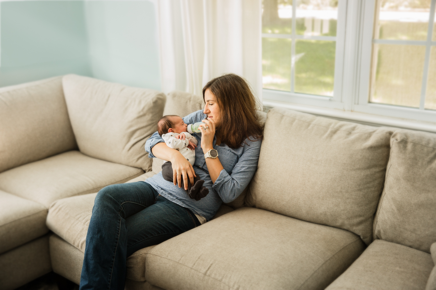 lifestyle photo of young mother holding her newborn baby by a window in family room
