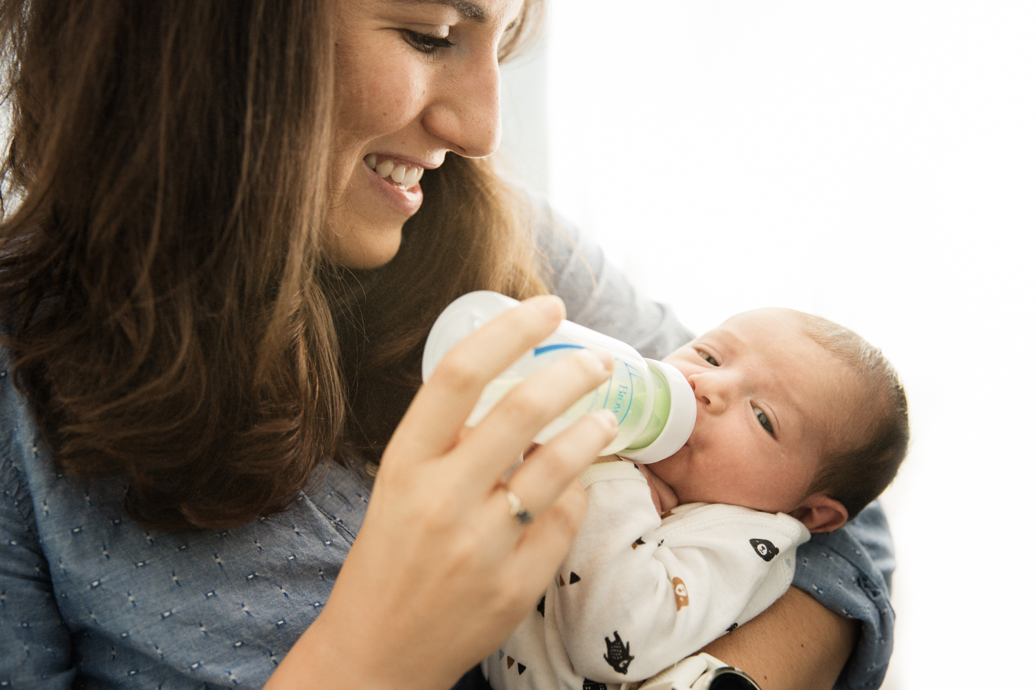 young smiling mother feeds infant daughter a bottle