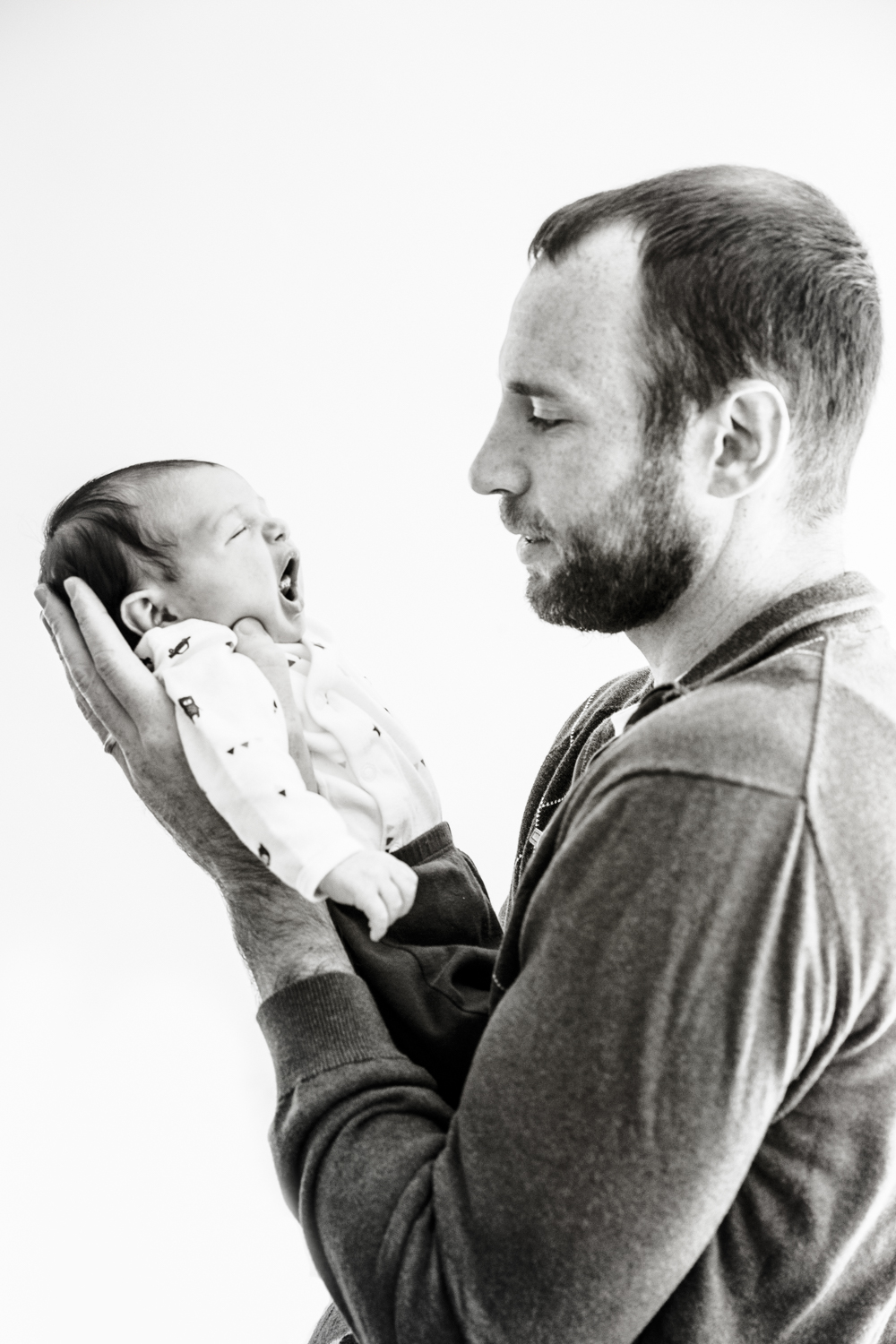 profile photograph in black and white of father holding his newborn girl up in his arms close to his face.