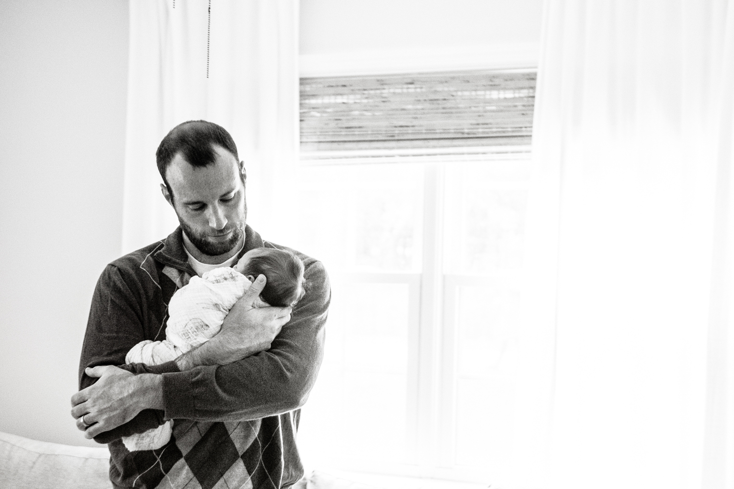 father holds infant daughter while standing by window in black and white photograph