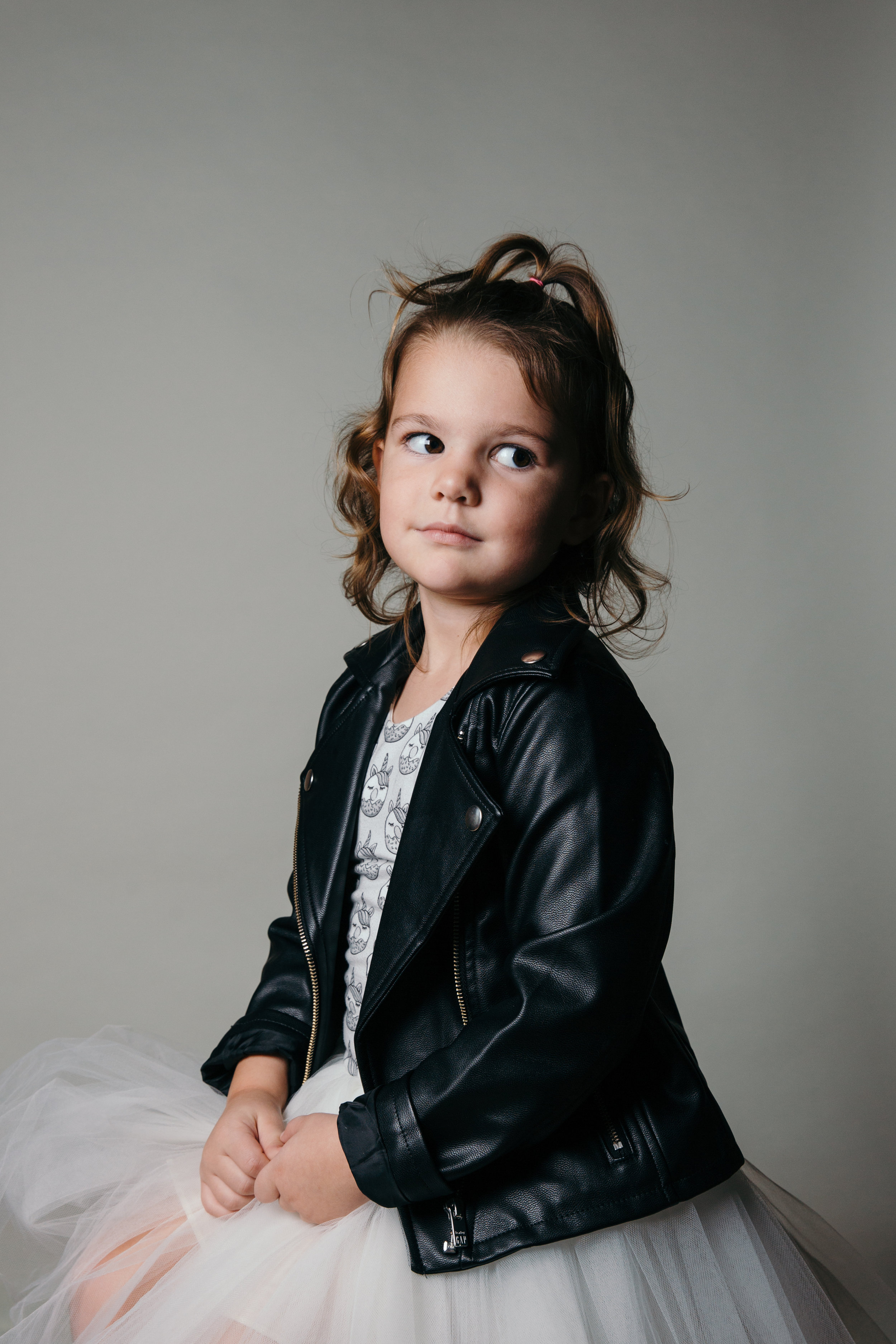 portrait of young girl sitting on stool in black jacket.