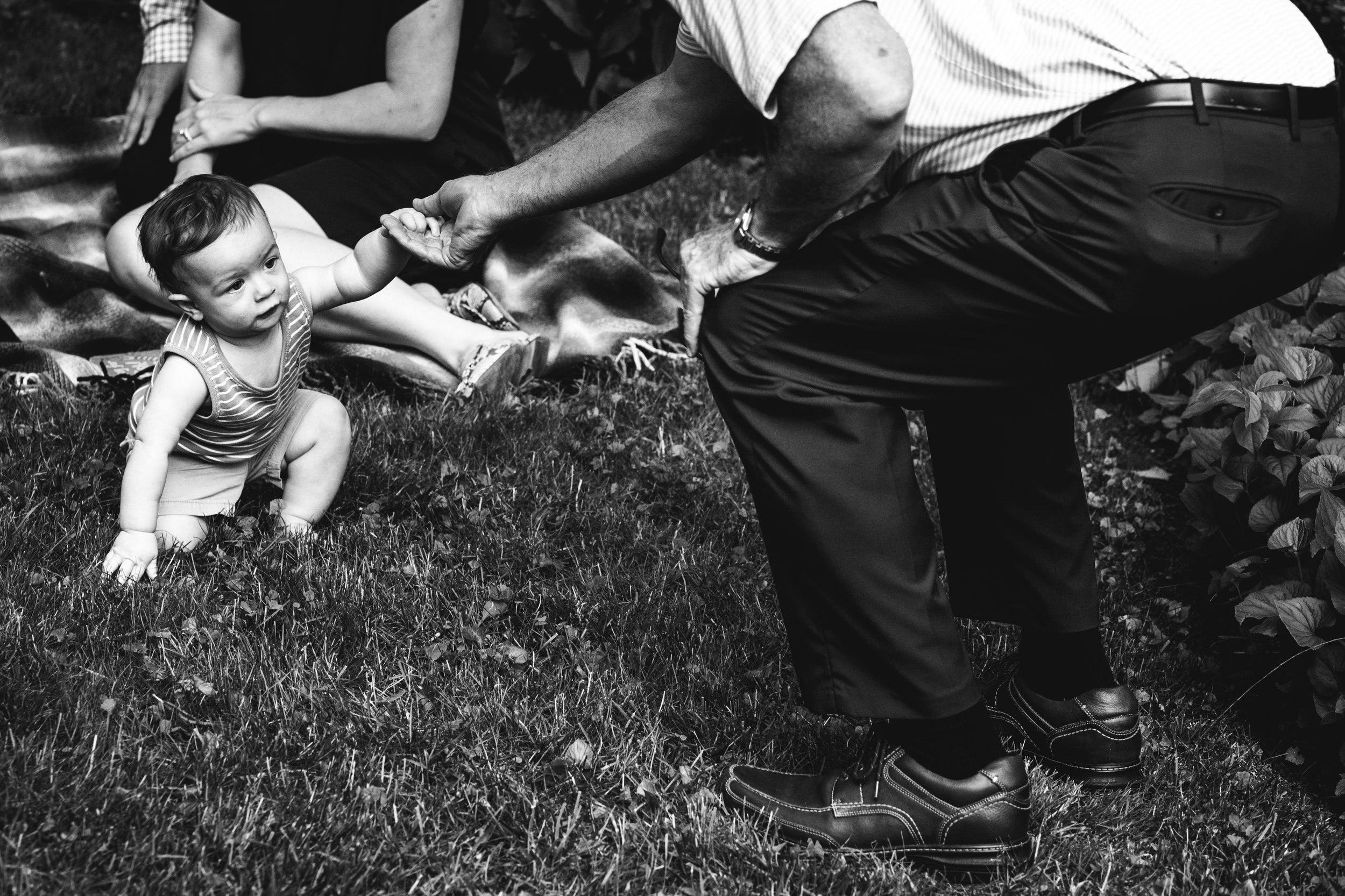 black and white photograph of father helping his son stand up to walk in the grass