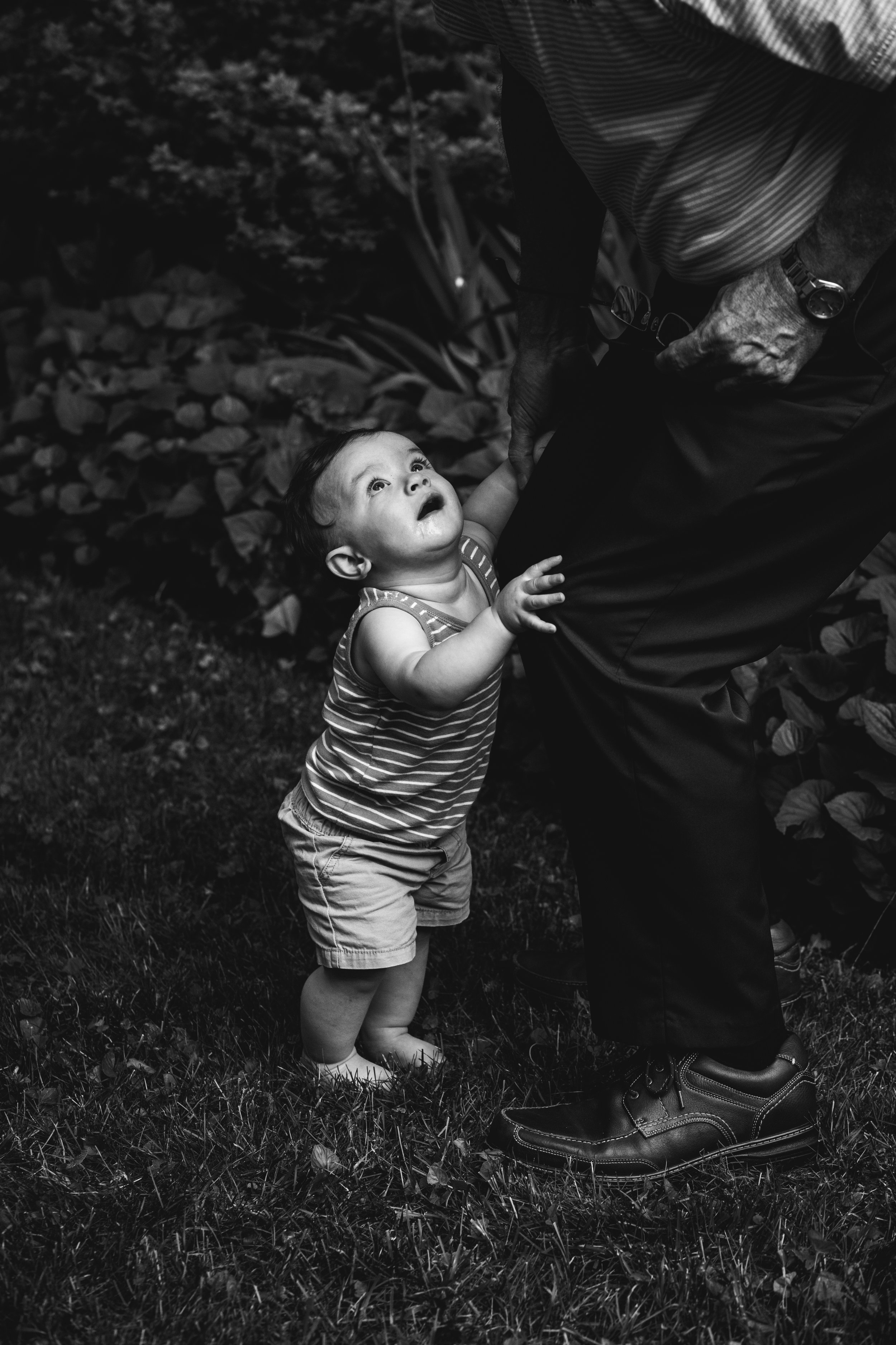 black and white photograph of toddler holding on to parent's let and looking up