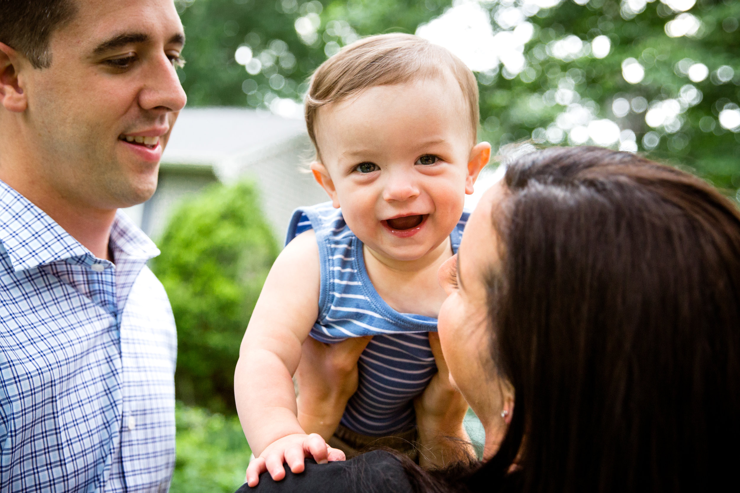 portrait of mom and dad with mom holding smiling young son towards camera