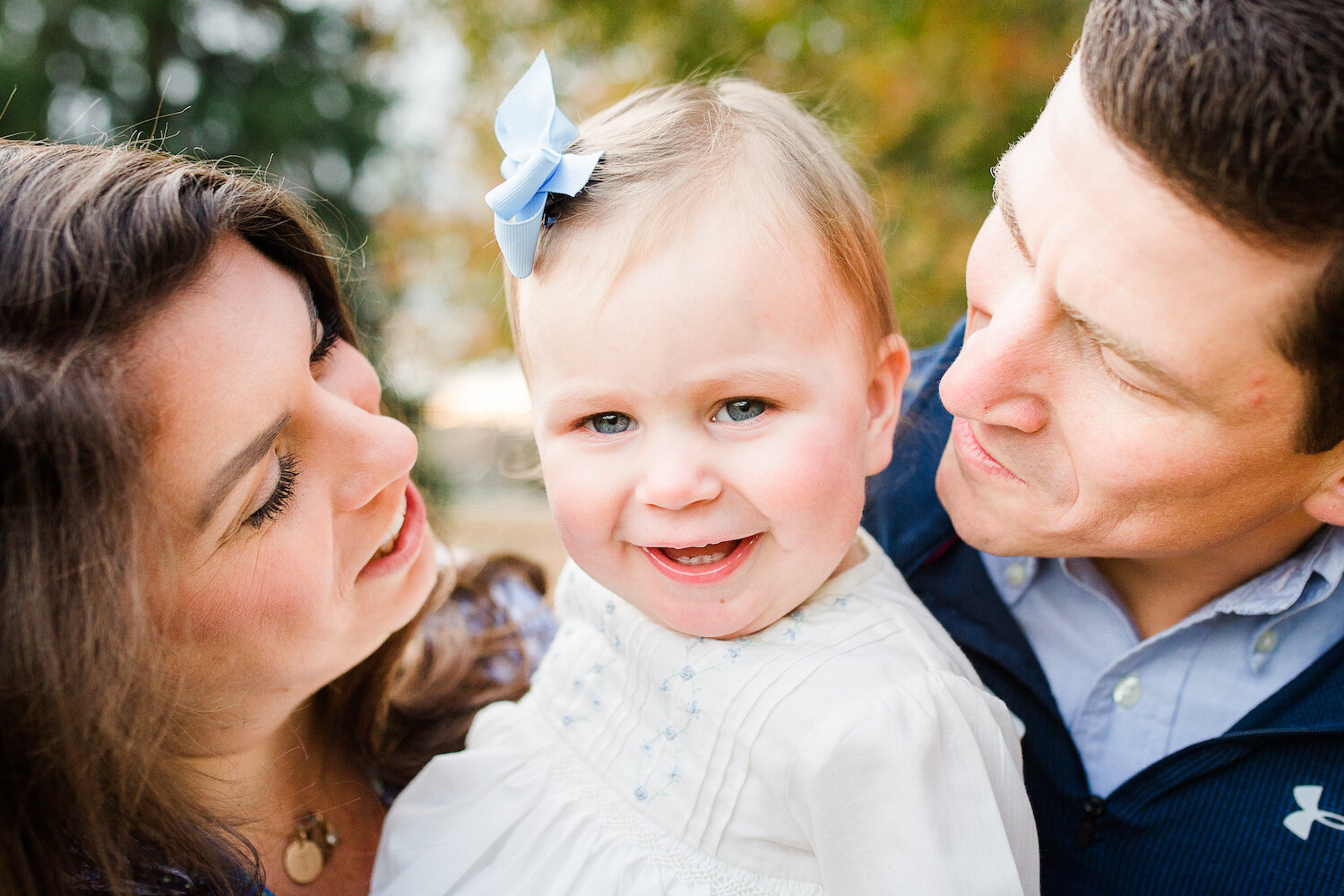parents smile at baby daughter wearing blue bow