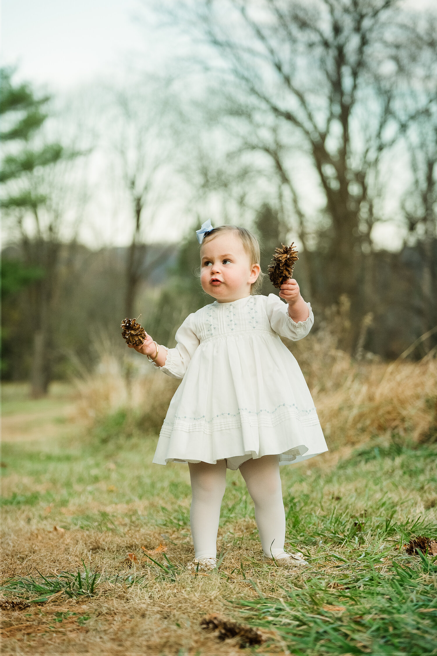 portrait of beautiful one year old girl in field holding pinecone.