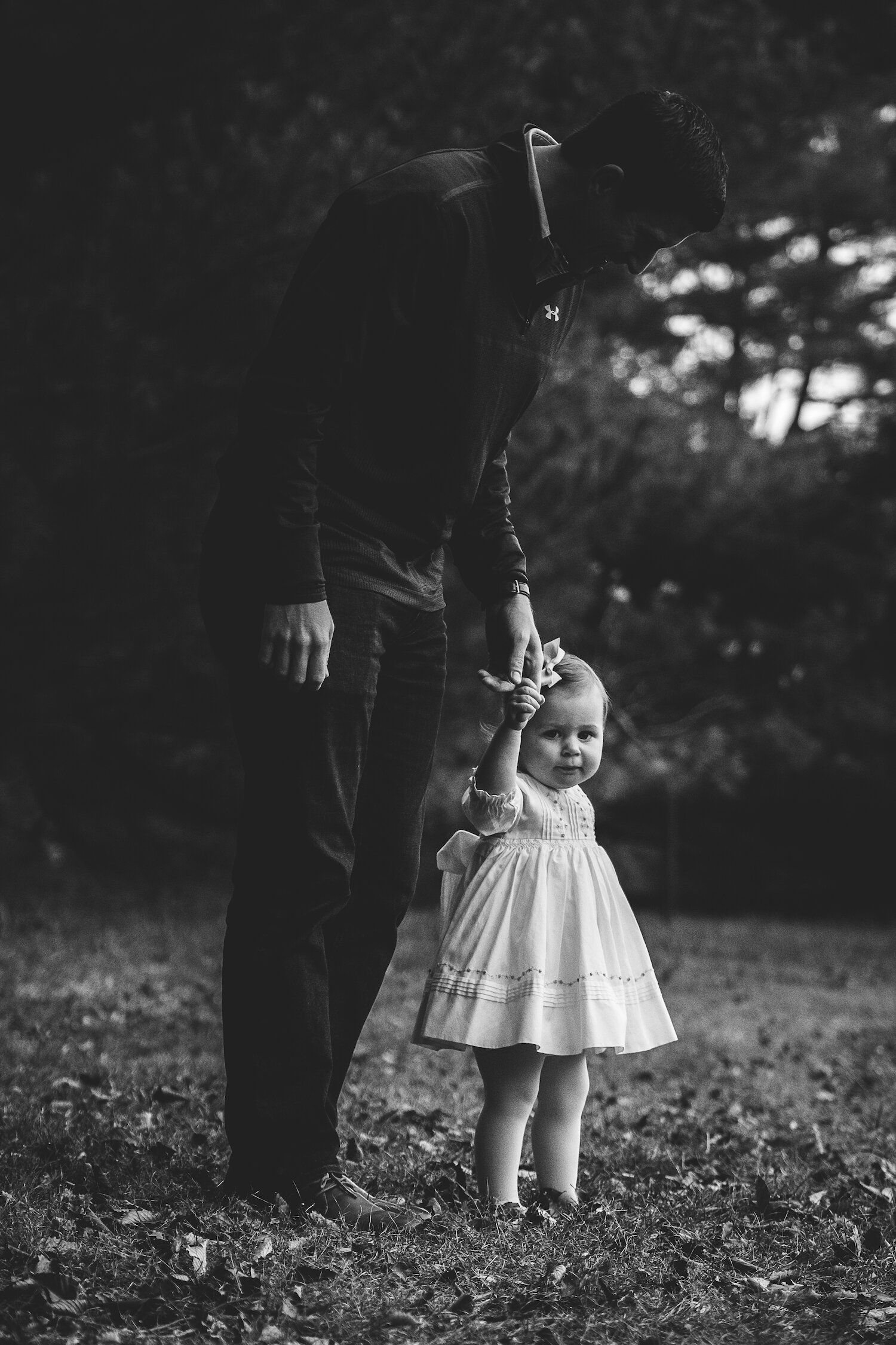 black and white photograph of little girl in white dress holding father's hand