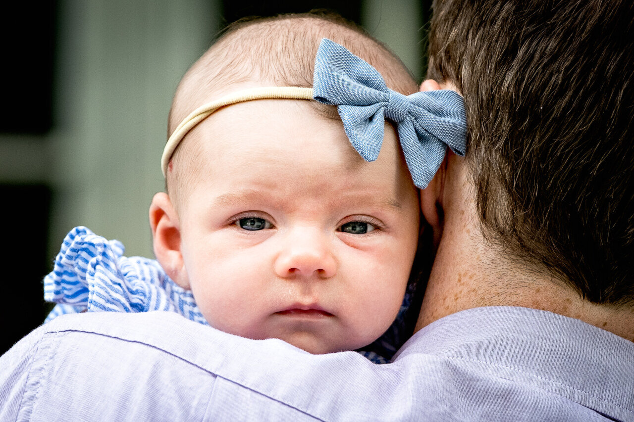 newborn_baby_girl_peeks_over_dads_shoulder_looking_at_camera.jpg