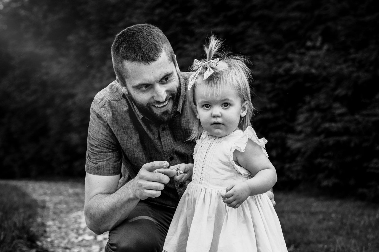 black and white image of father smiling t one year old daughter while walking on outdoor park path.