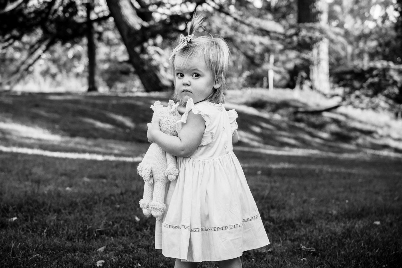 black and white photograph of one year old child holding toy stuffed animal and looking suspiciously at the camera