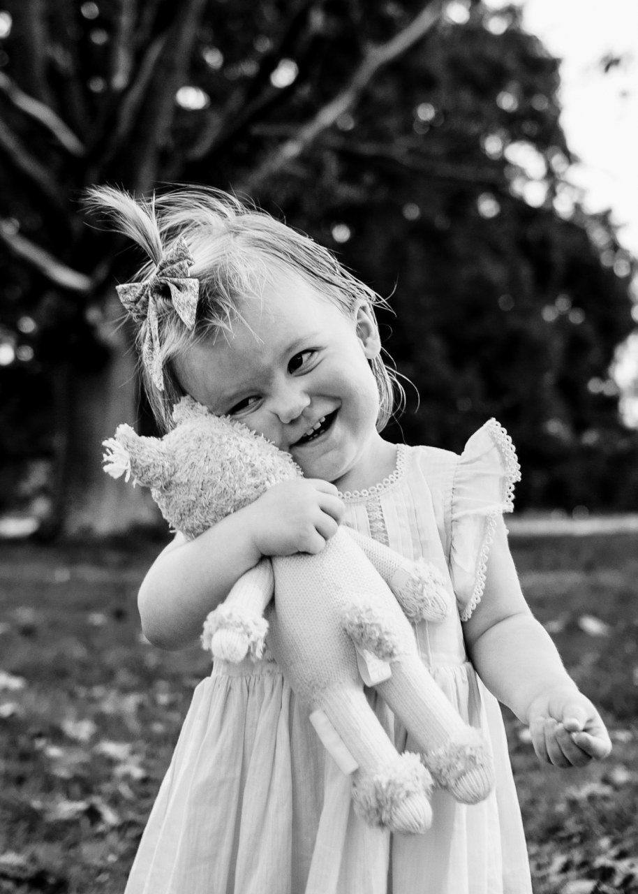 beautiful black and white portrait of one year old girl smiling and hugging her favorite stuffed animal 