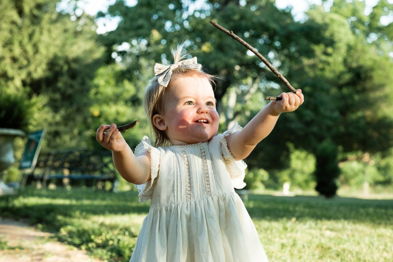 smiling toddler girl holds a stick to present it to her parents in candid family photograph