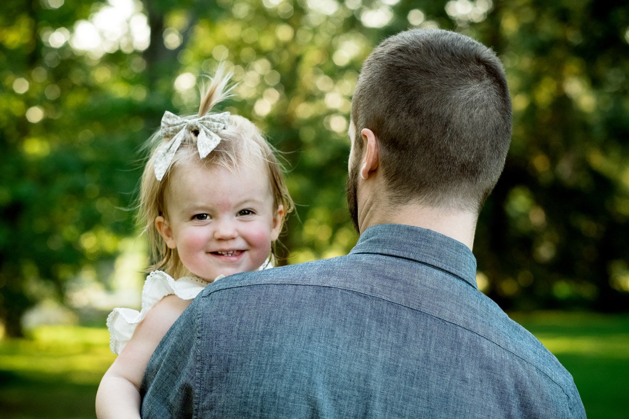 one year old child smiles over father's shoulder 