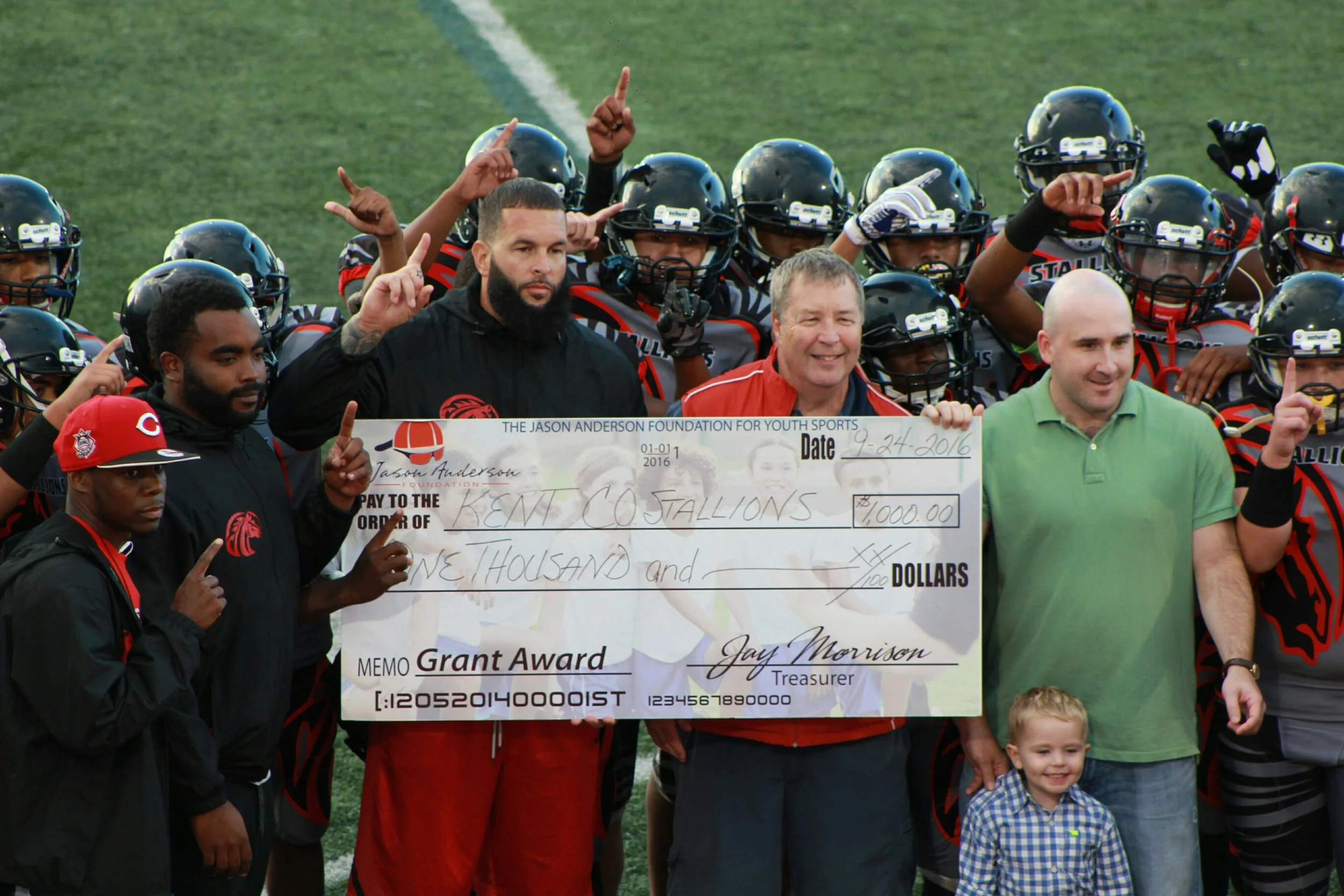 Marc Anderson, President of the foundation, Andrew Schwab, Board Chair and Jason’s son Ryan, present a $1,000 check to the Kent County Stallions prior to a September 2016 game.