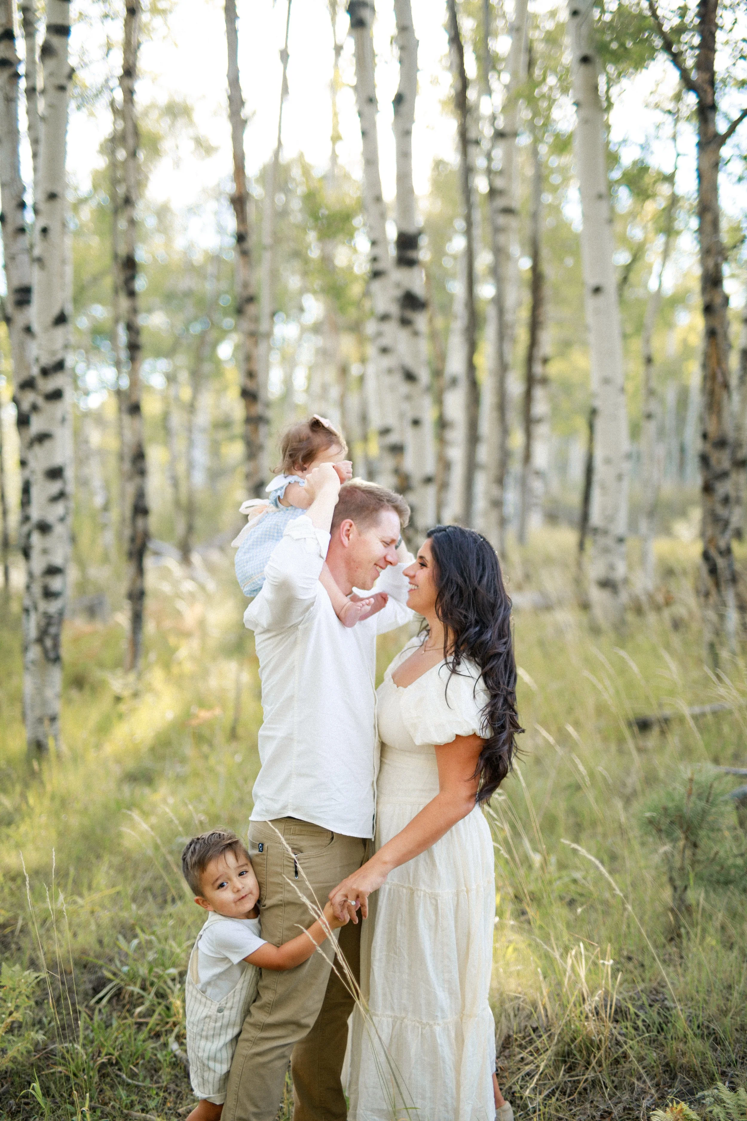 Family of four enjoying time outdoors in a forest of tall, white-barked trees, with sunlight filtering through the leaves.