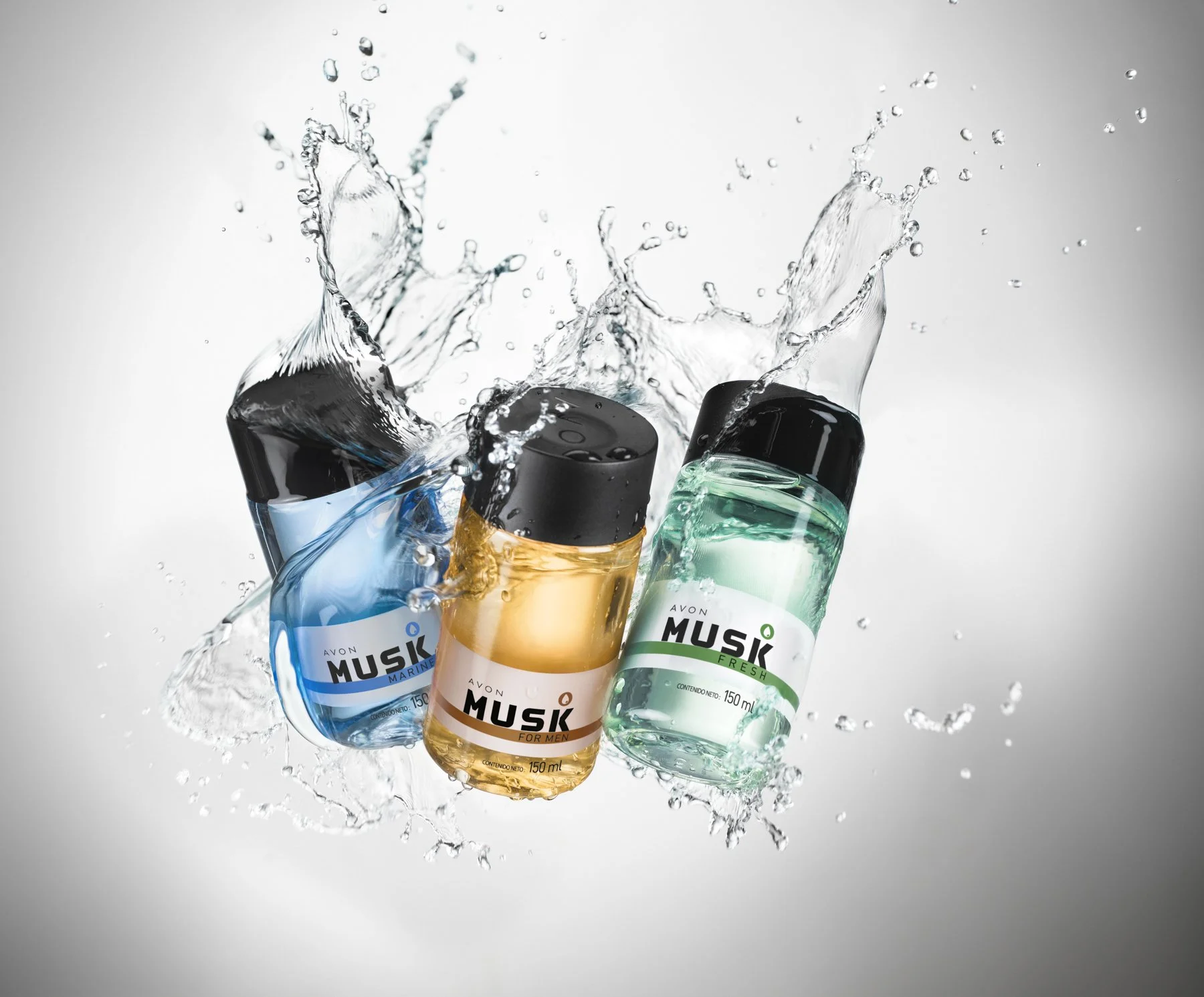 Tres botellas de productos de cuidado personal de la marca Musk, con agua salpicada en el aire, fondo gris.