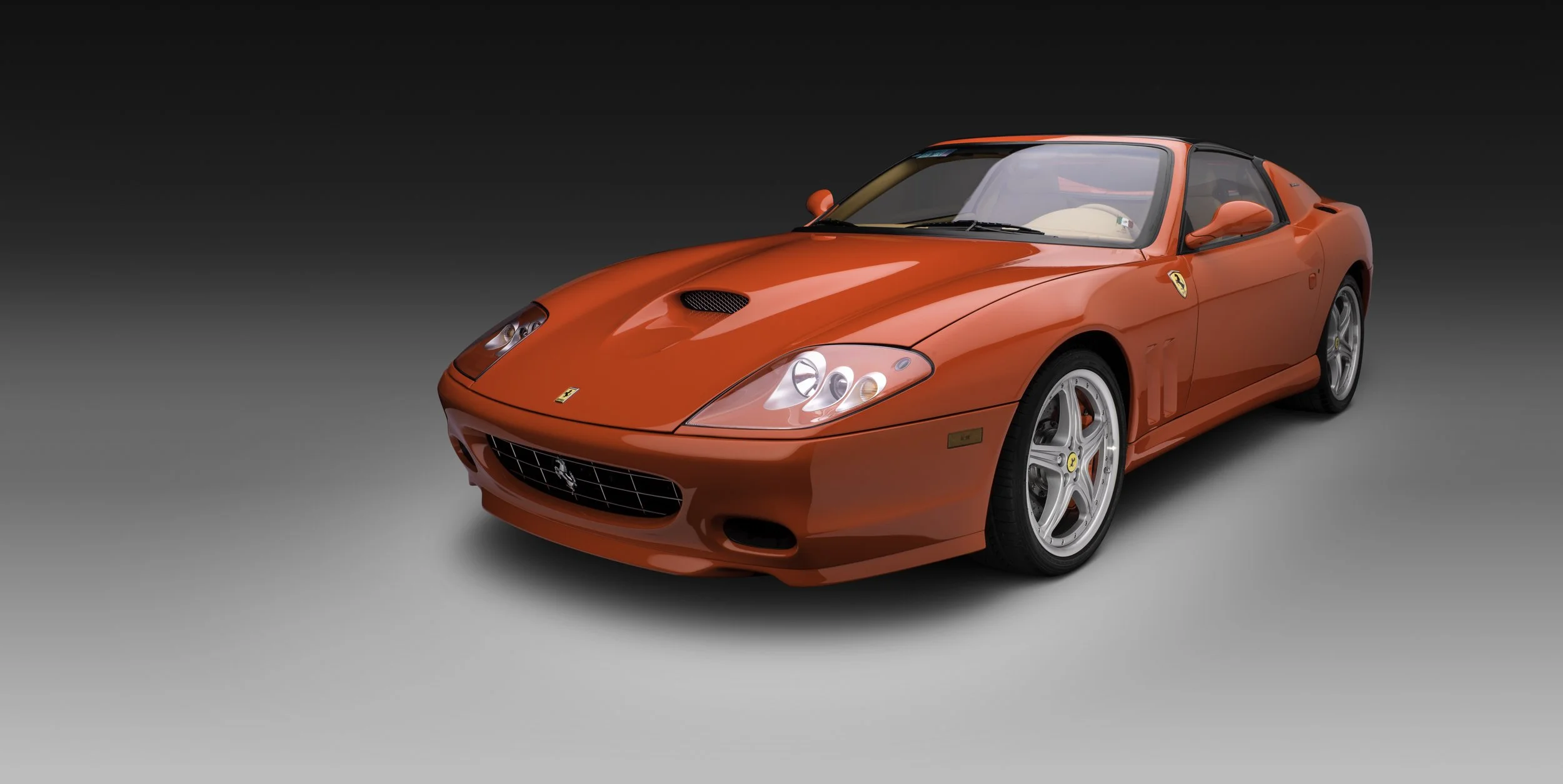 Auto deportivo rojo marca Ferrari, vista frontal en un fondo gris oscuro.