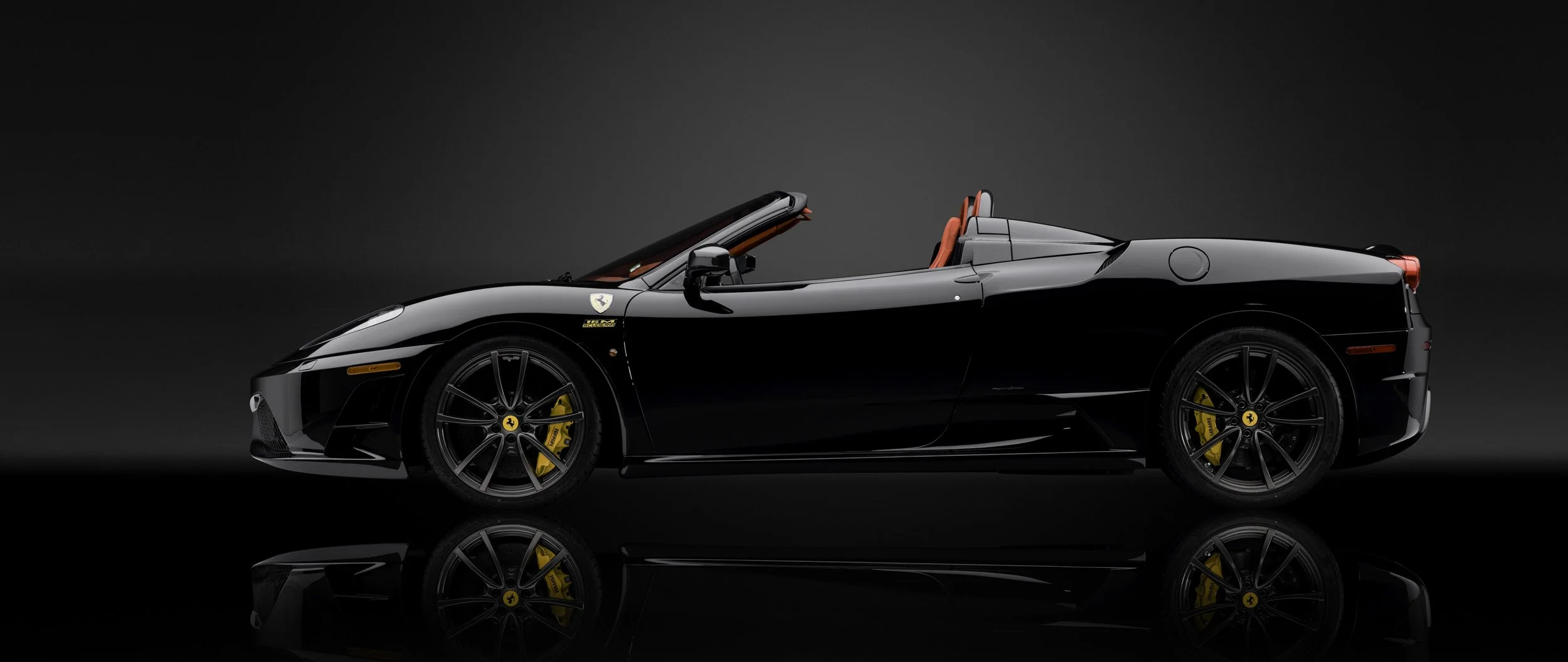 Coches negro Ferrari descapotable con llantas doradas y freno de disco calipers amarillos en un fondo oscuro.
