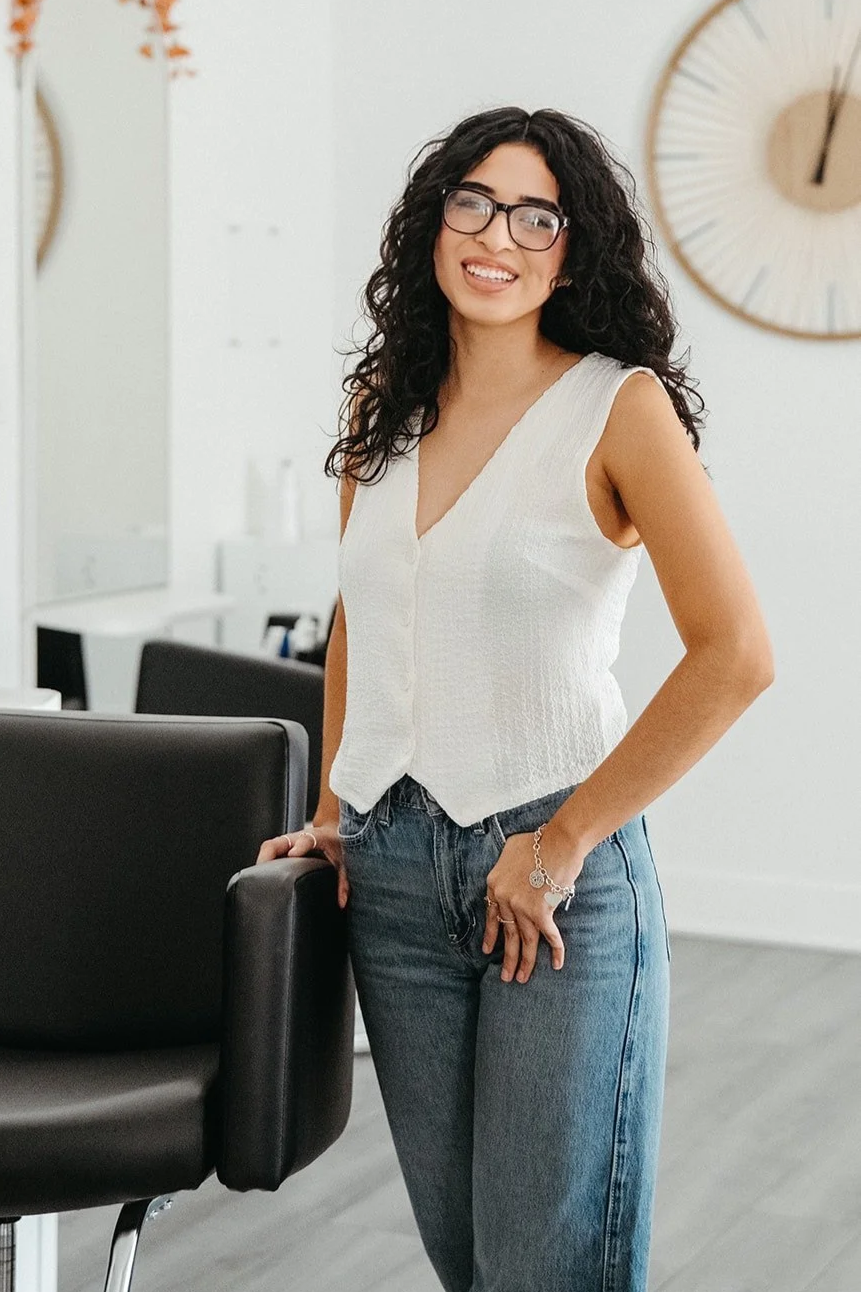 Jasmine, a Siren hairstylist, smiling while standing beside a salon chair inside Siren Curl Studio.