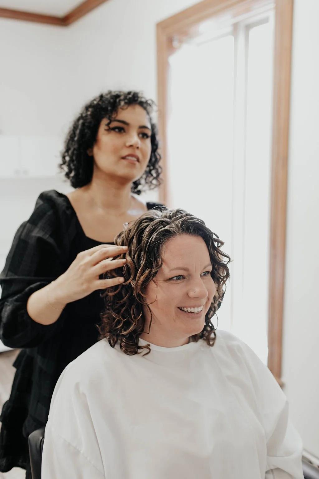 Shirin and her curly-haired client smiling together as Shirin adds the finishing touches to the client’s beautifully defined curls at Siren Curl Studio.