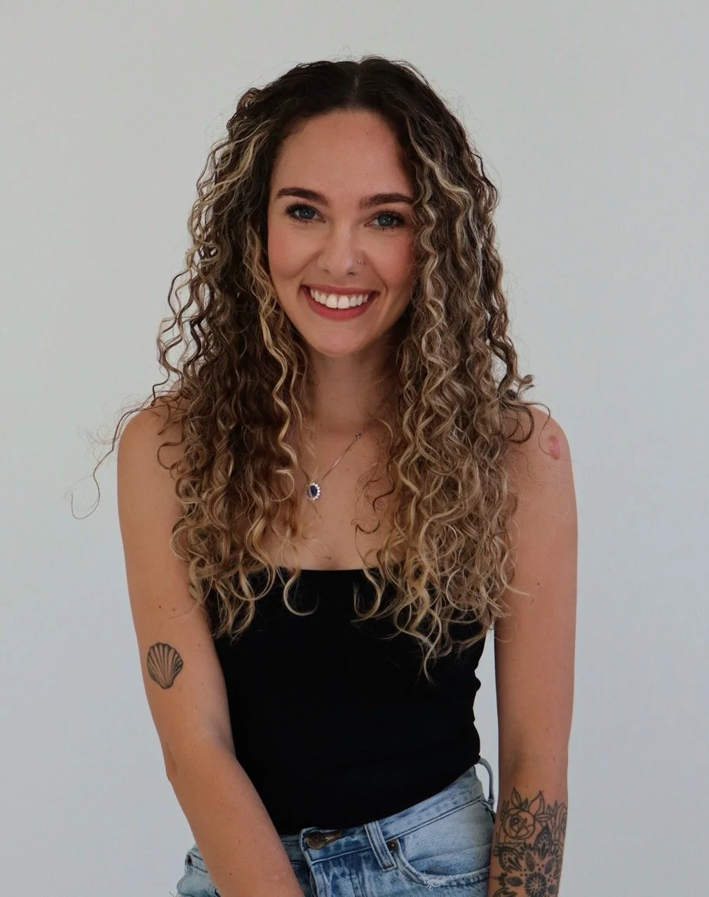 Ally, the operations manager at Siren Curl Studio, smiling with her beautiful curls in a professional portrait with a gray background.