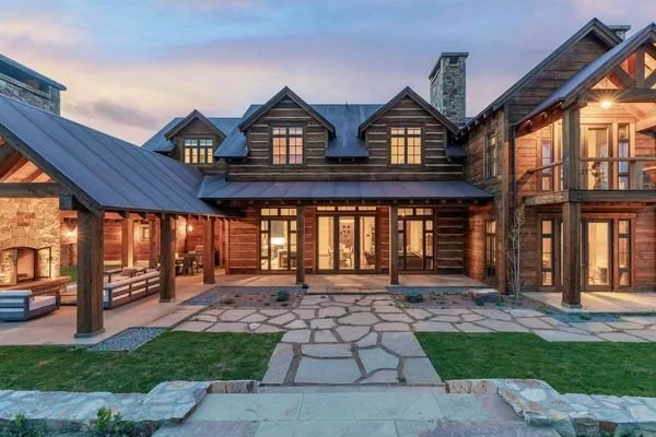 A large, multi-story custom house made of brick and wood with a stone pathway leading to the entrance, surrounded by a well-kept lawn and outdoor seating areas, during sunset.  Built in the Telluride CO area.